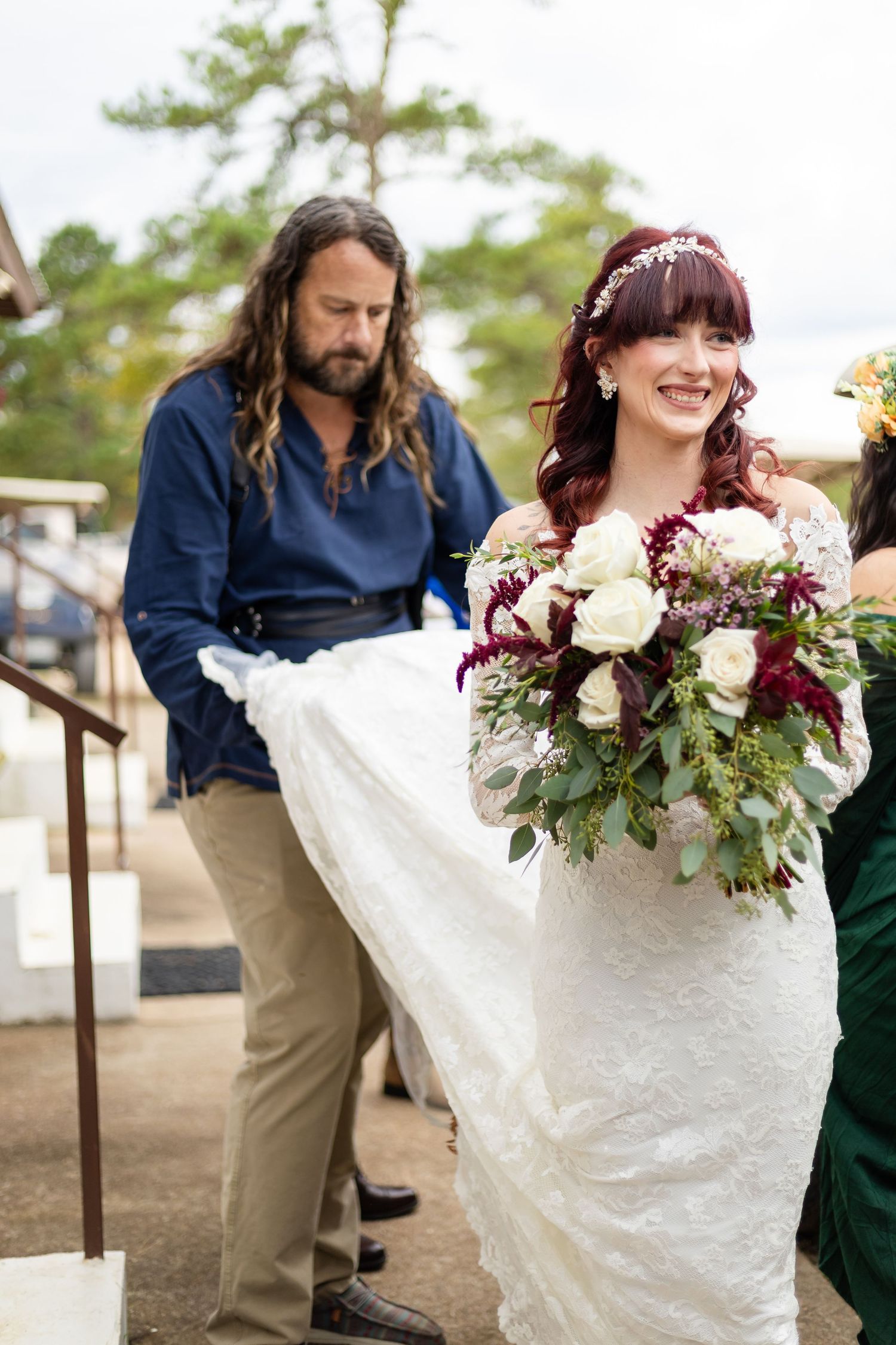 Wedding party members in navy and forest green attire pose outdoors with burgundy and white floral bouquets.