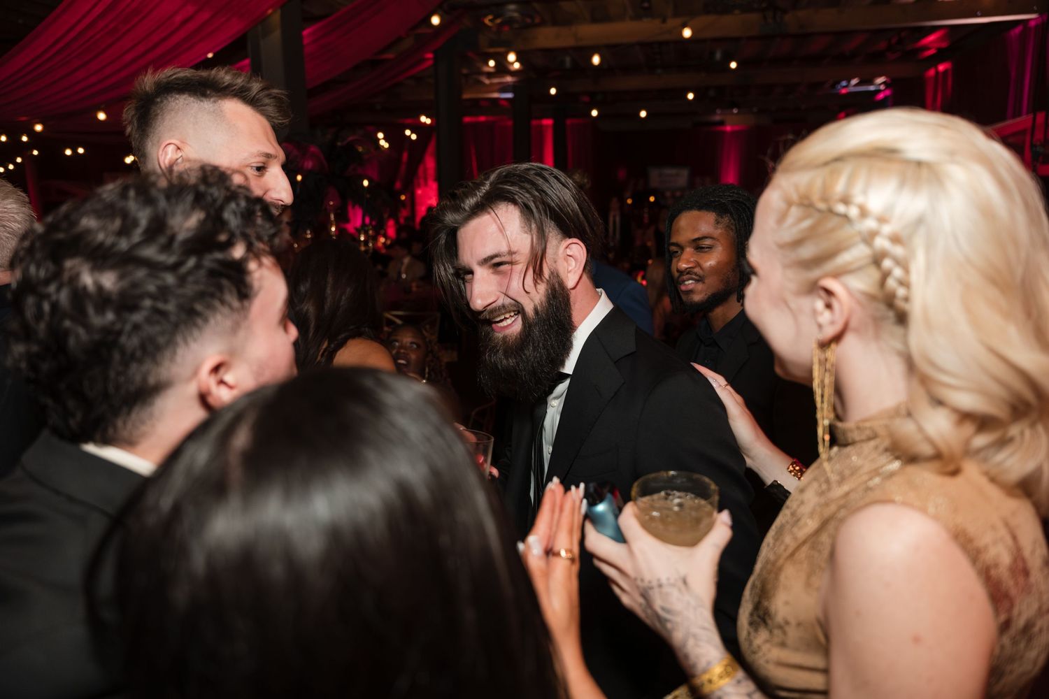 People dancing and socializing at a dimly lit nightclub with red lighting and festive atmosphere.