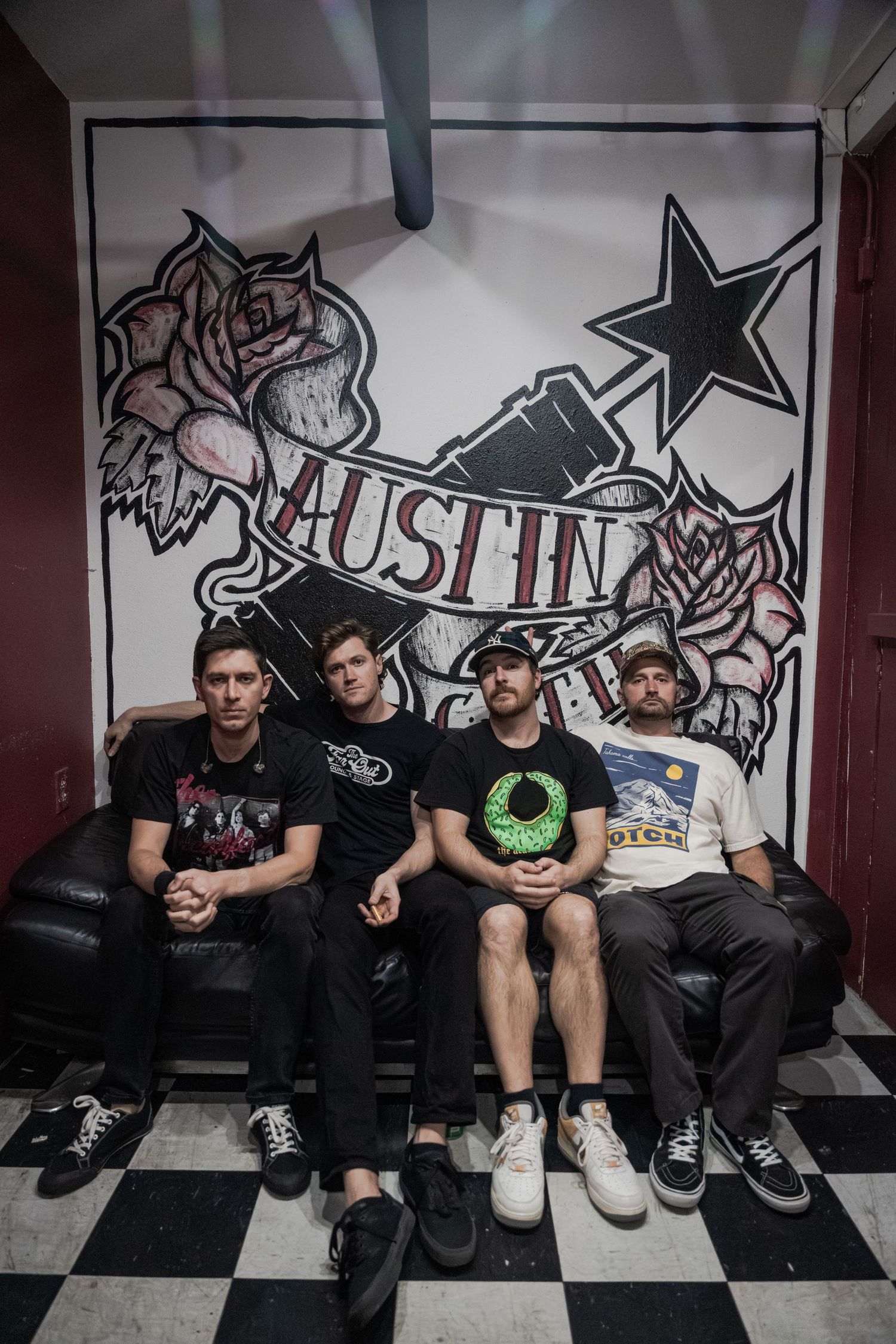 A group sits on a bench against a wall with graffiti art and star designs in a black and white checkered room.