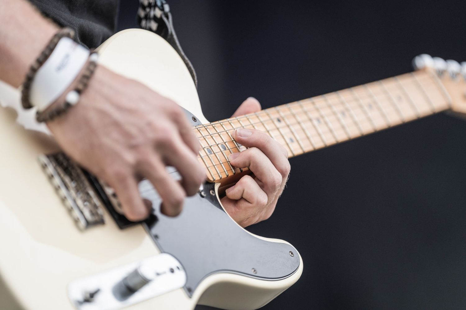 Close-up view of hands playing an electric guitar with silver pickups and maple fretboard.