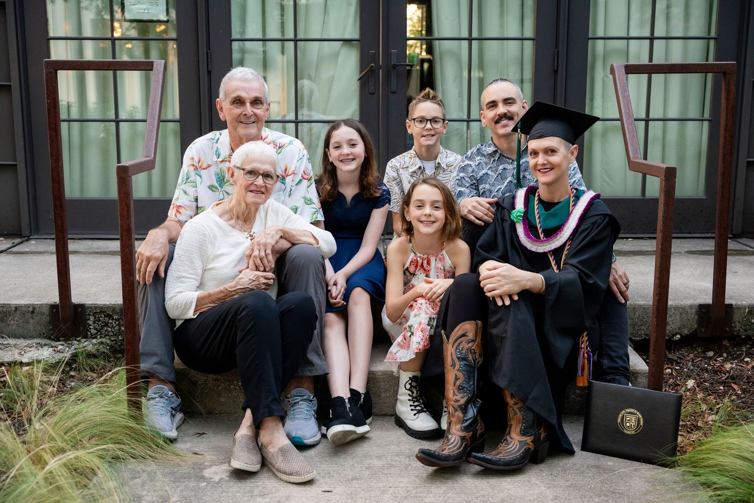 A family group sits together on outdoor steps with a brown dog, sharing a happy moment in casual attire.