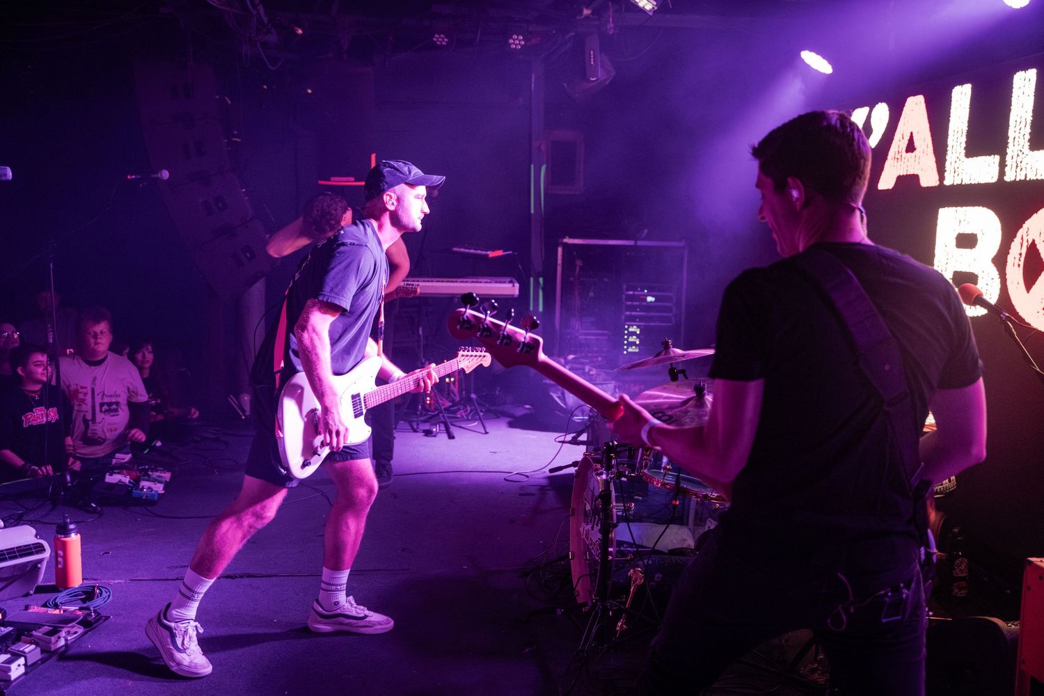 Band performing on stage with electric guitars under purple stage lighting at a live music venue concert.