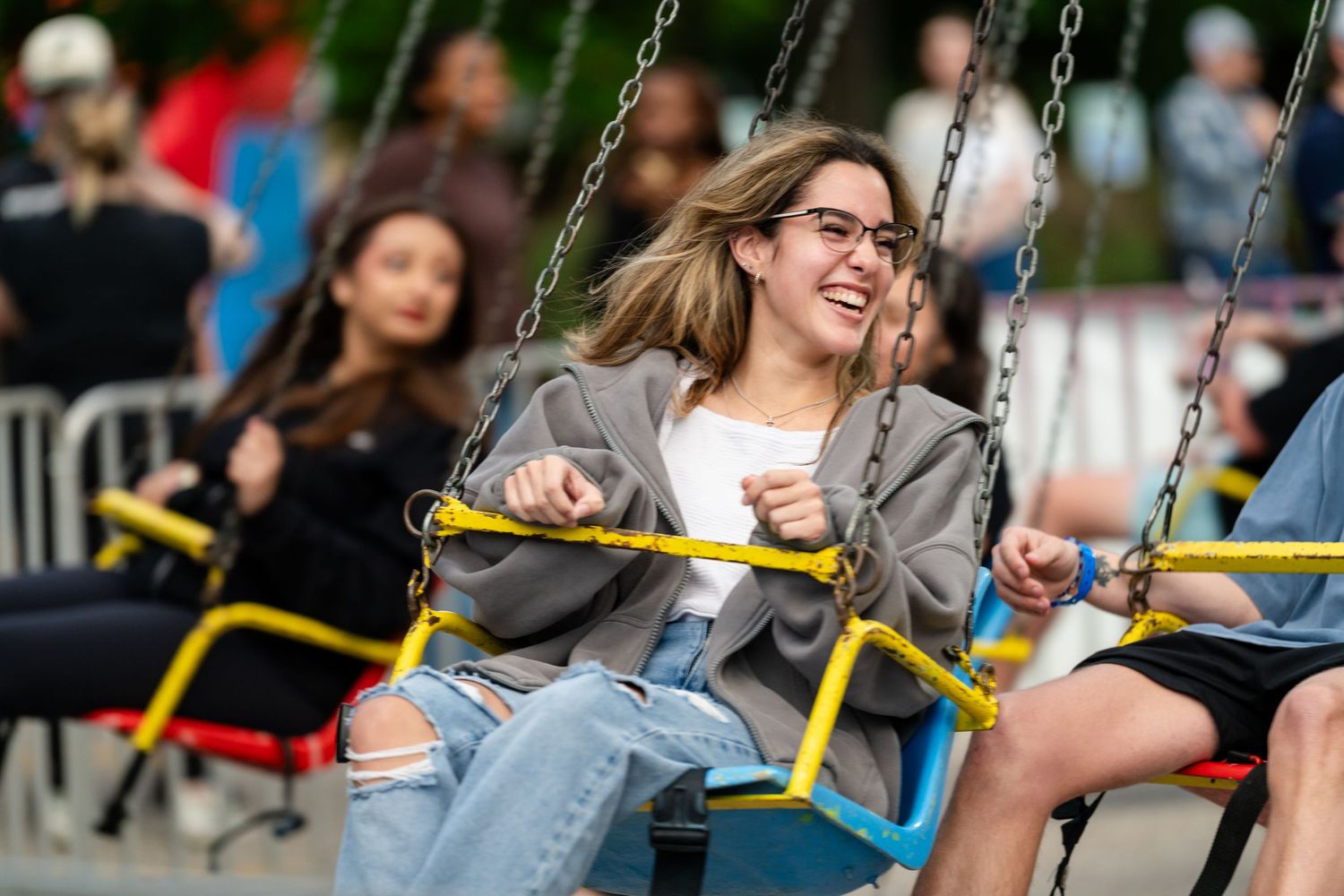 Young woman laughing joyfully on a chain swing ride at an outdoor amusement park or fair.