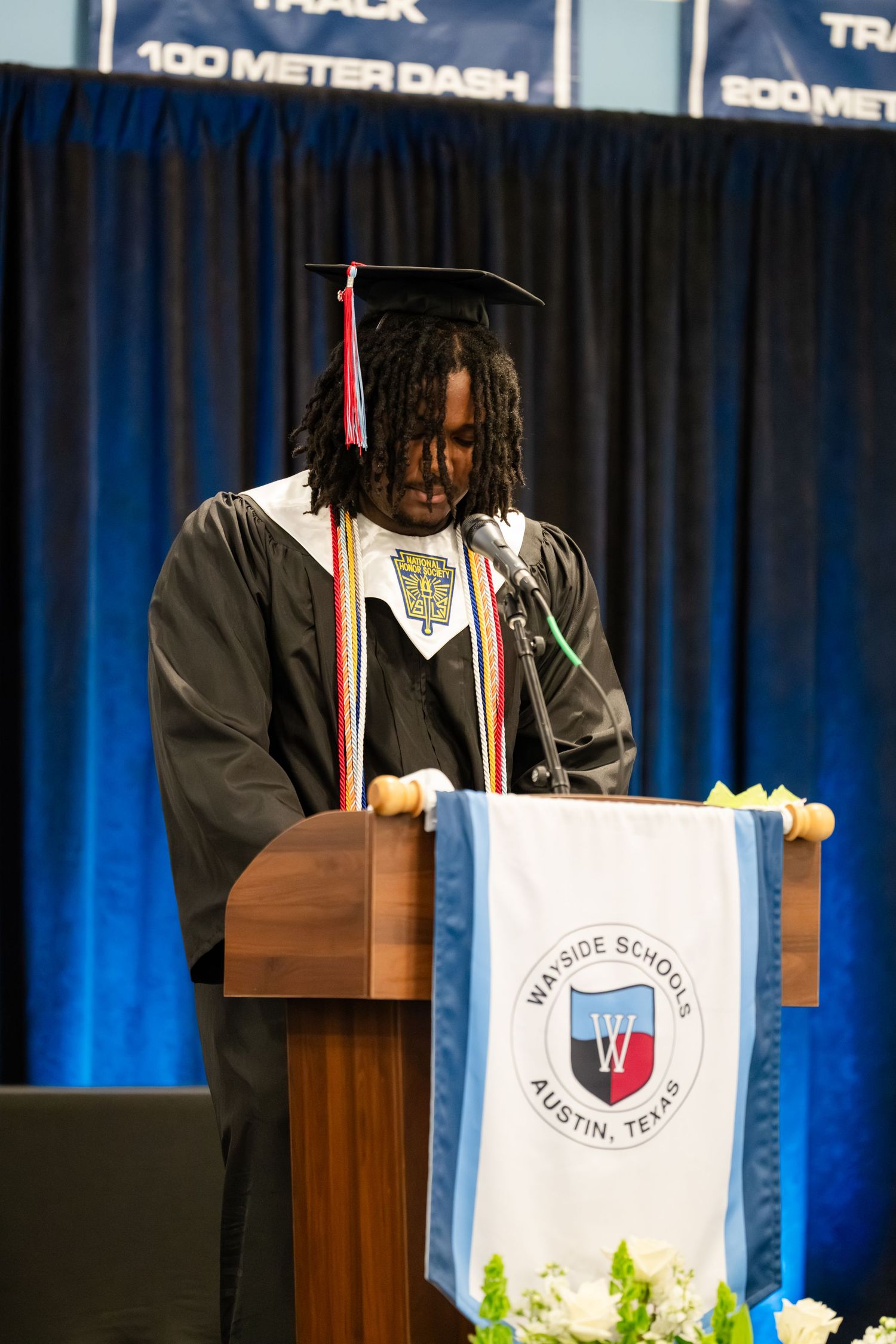 Graduate in cap and gown speaks at podium during Wayside Schools Austin Texas graduation ceremony.