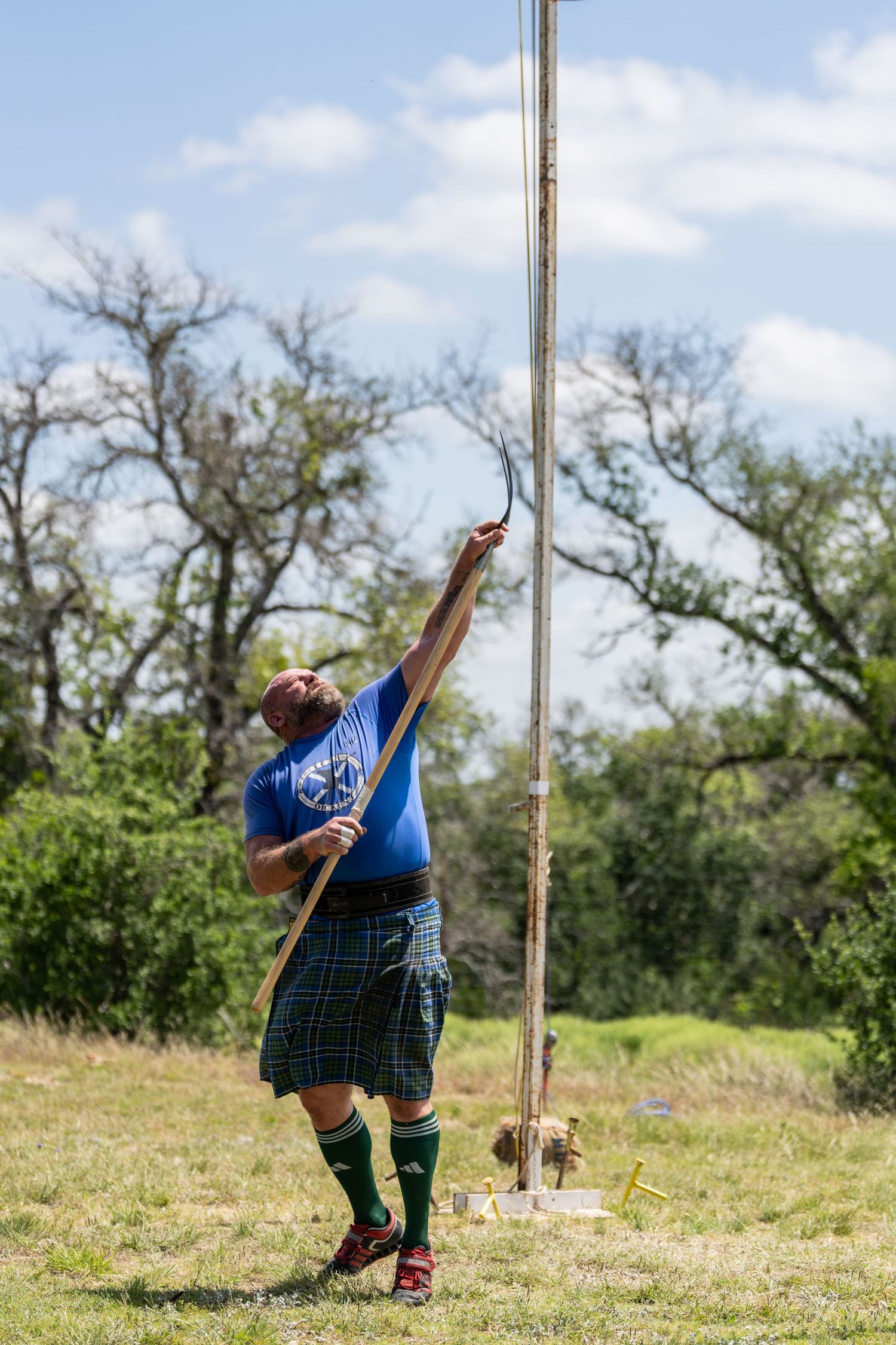 Man in kilt and blue shirt tossing caber at Scottish Highland Games outdoors.