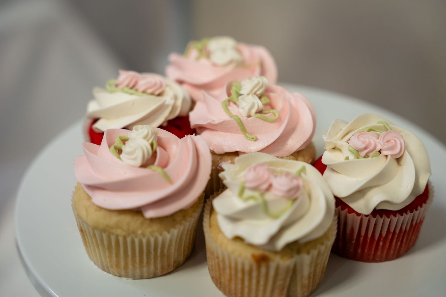 Elegant pink and white frosted cupcakes with rose decorations displayed on a white cake stand.