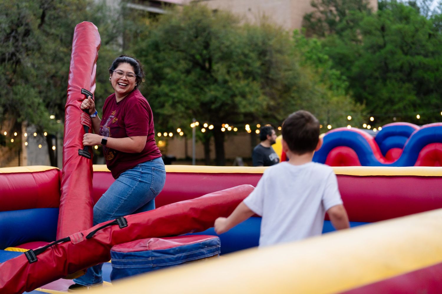 Two people enjoying an inflatable obstacle course at an outdoor evening event with string lights.