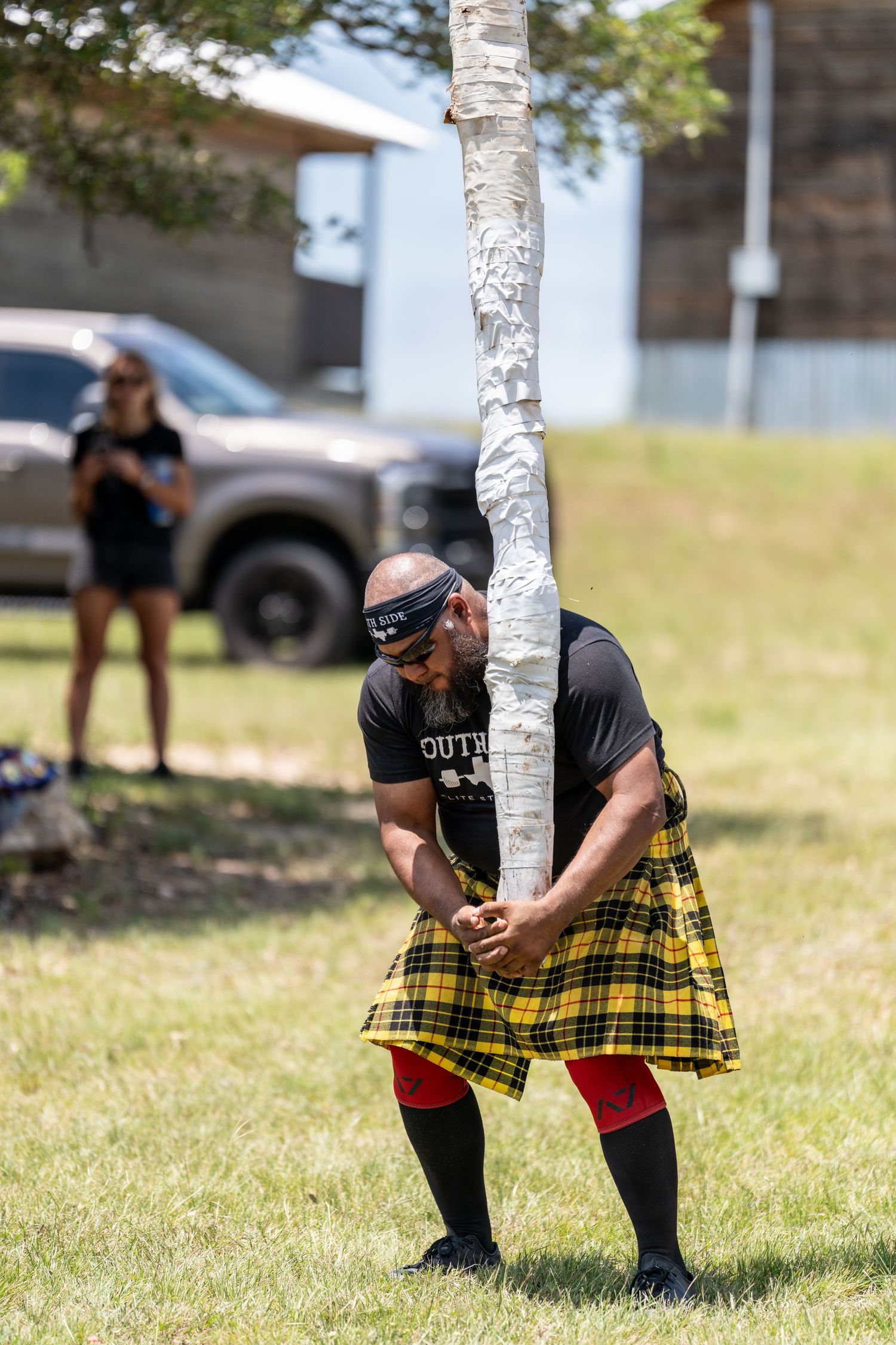 Man in yellow tartan kilt tossing a caber at a Highland Games competition outdoors.