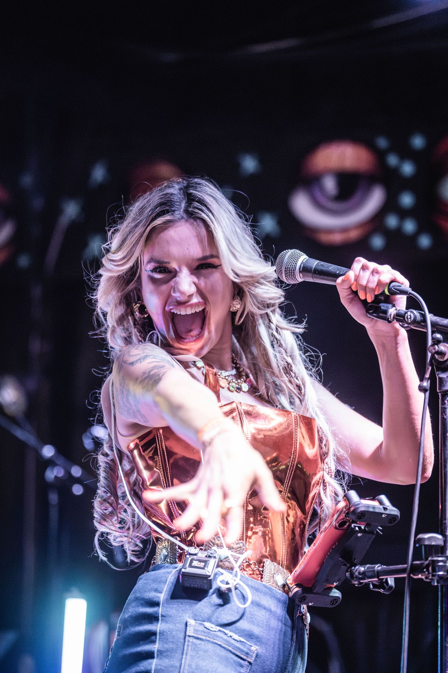 Energetic performer with blonde hair sings passionately on stage with dramatic lighting and microphone in hand.