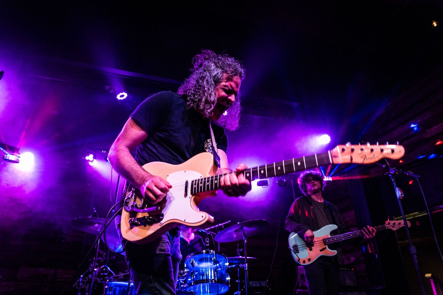Guitarist performs on stage with electric guitar under dramatic purple stage lighting during live concert performance.
