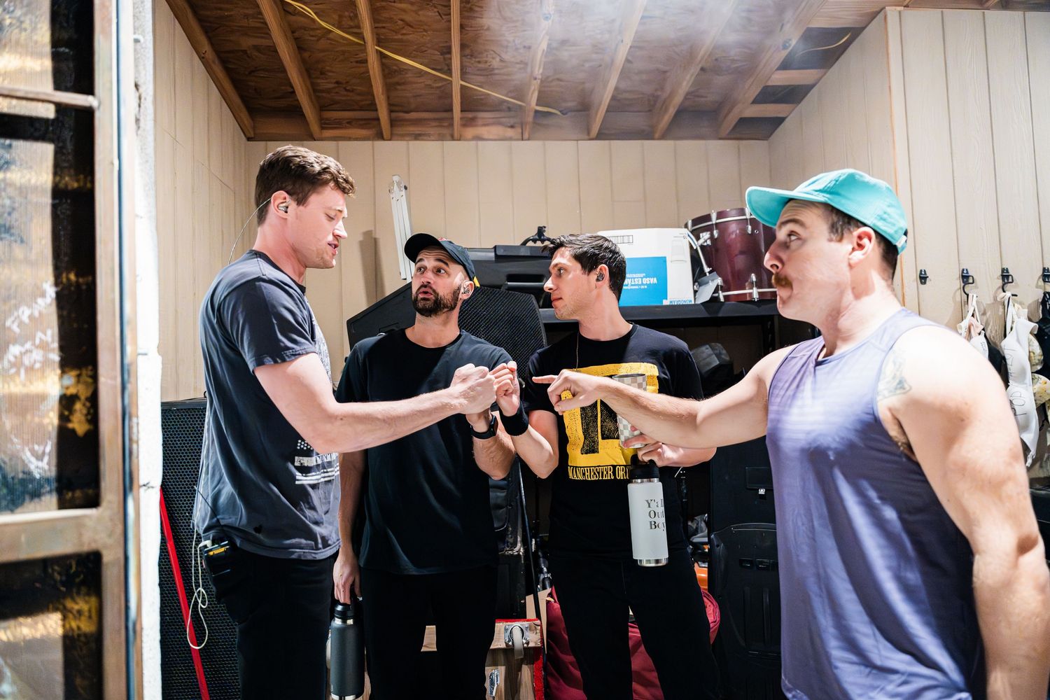 Band members interact backstage before a performance surrounded by equipment and gear.