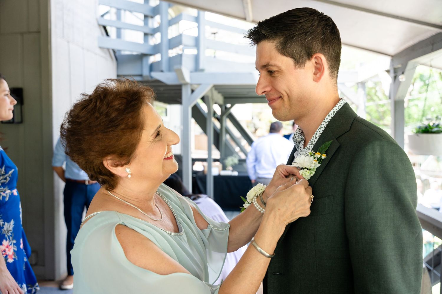 Boutonniere being pinned on formal green suit jacket during wedding preparation.