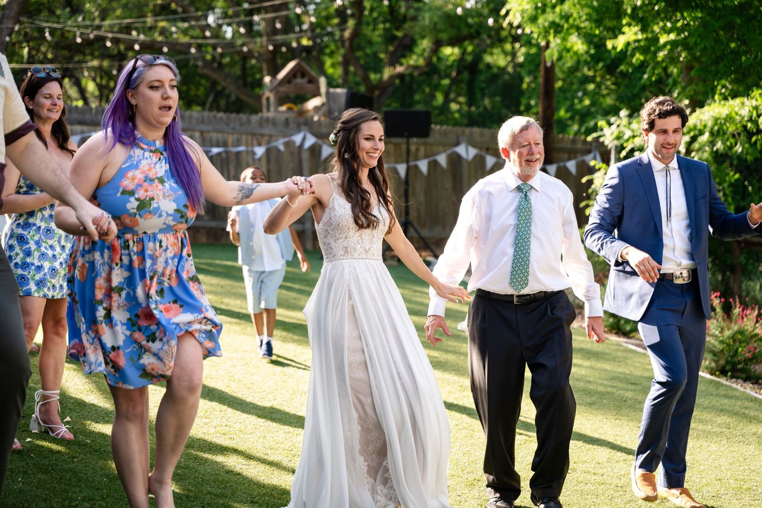 Wedding guests dance together on a lawn with string lights and trees in the background.