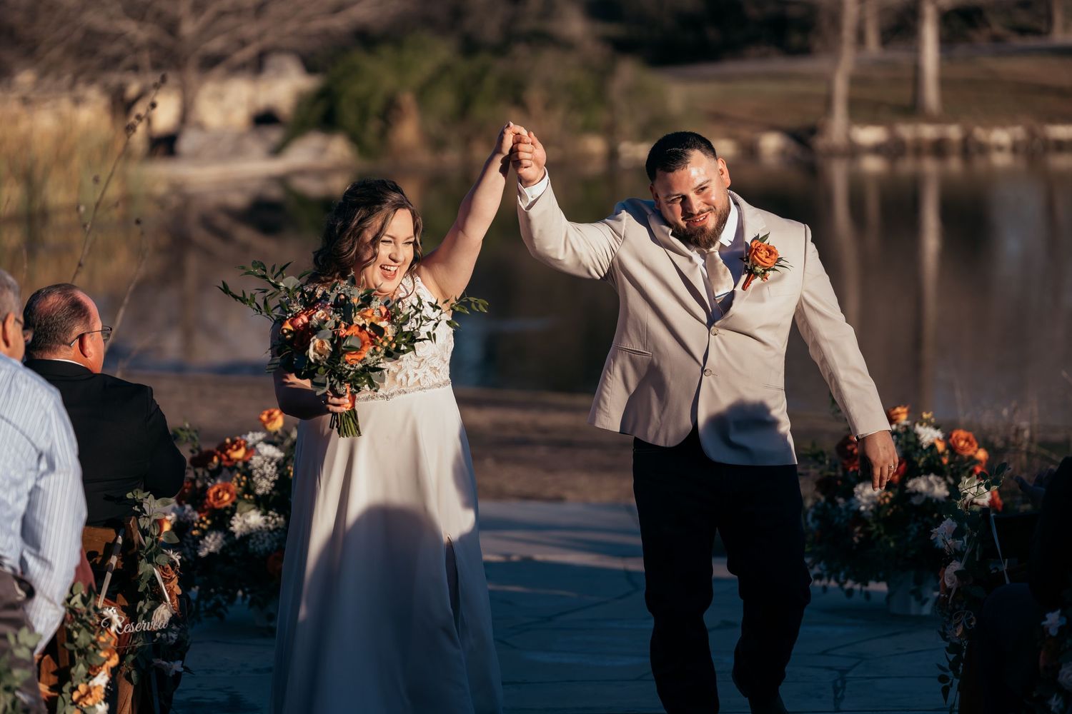 Newlyweds celebrate with raised hands on a dock decorated with fall floral arrangements.