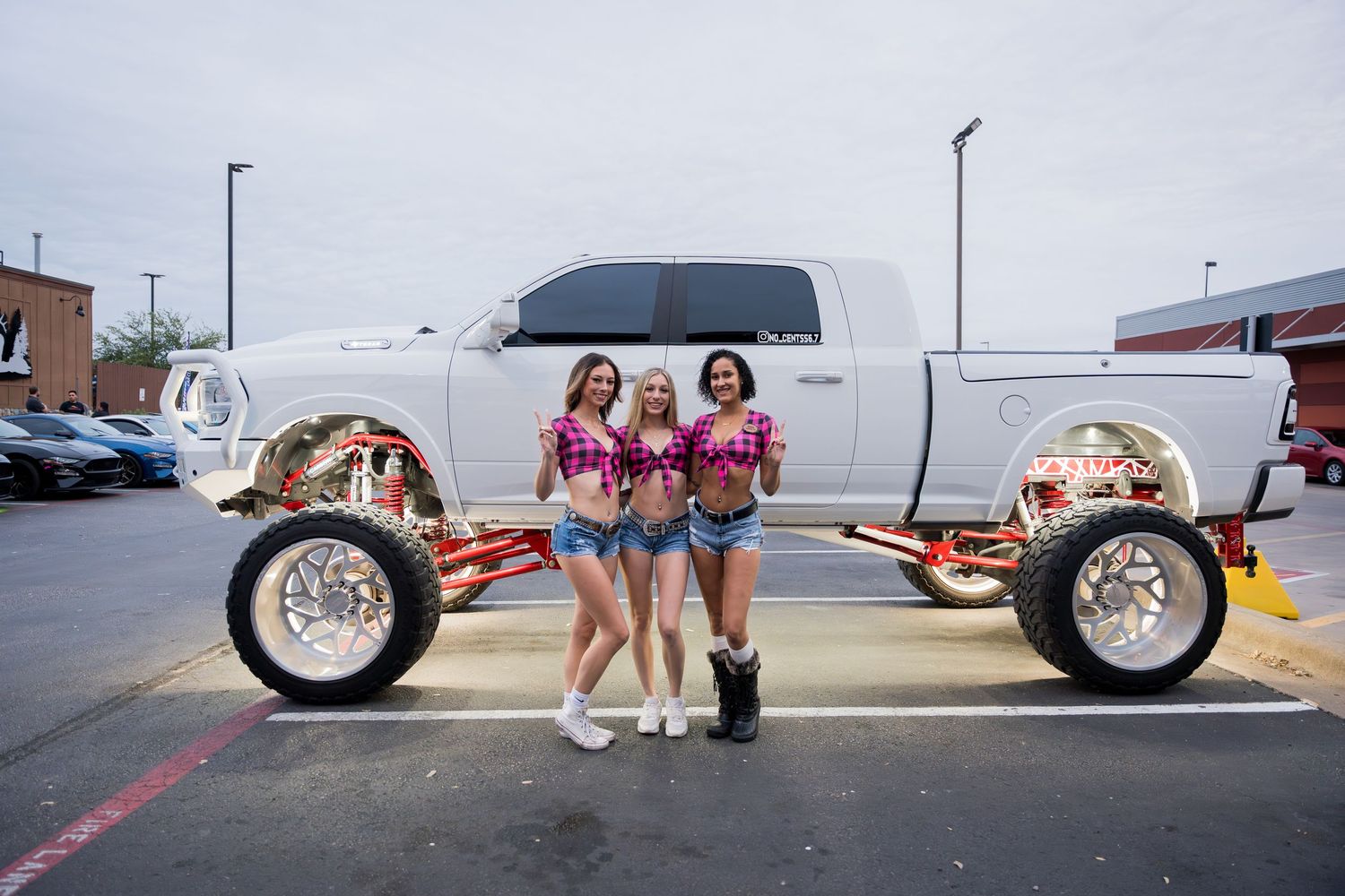Models pose with a custom lifted white truck chassis in a parking lot.