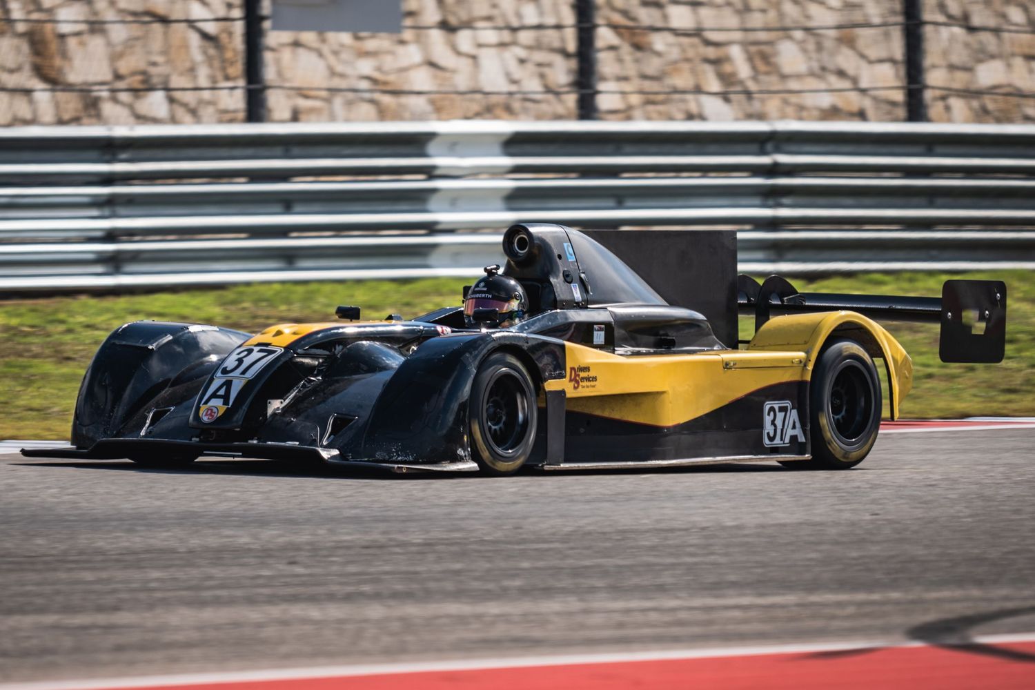 Black prototype race car corners at high speed on a professional racing circuit.
