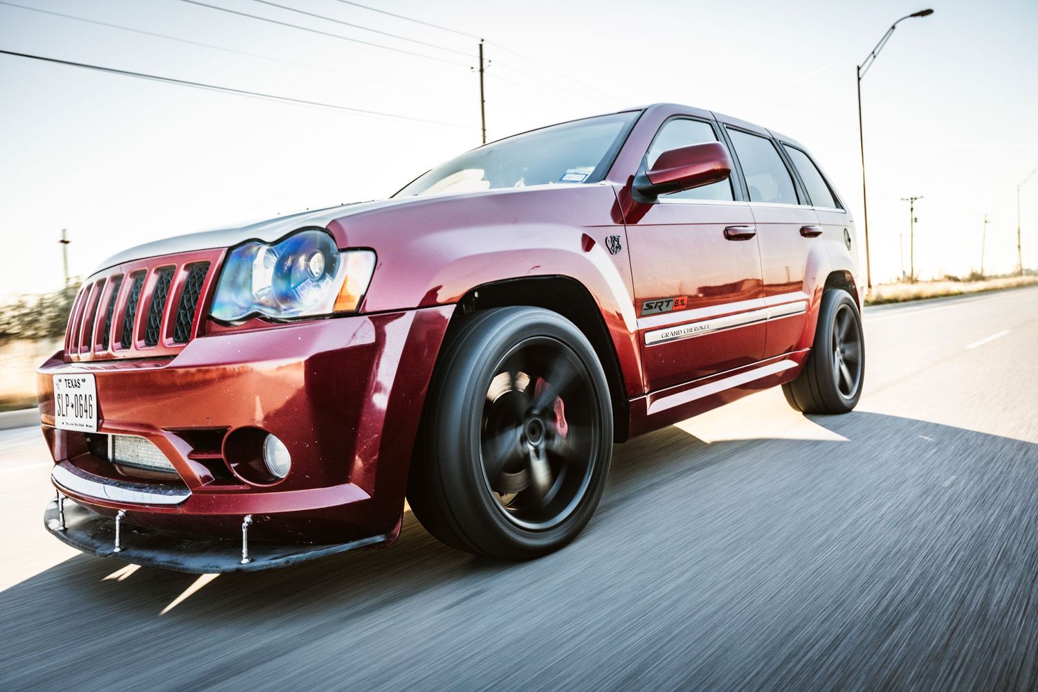Red Jeep Grand Cherokee SRT8 with aggressive body kit captured in dynamic driving shot.
