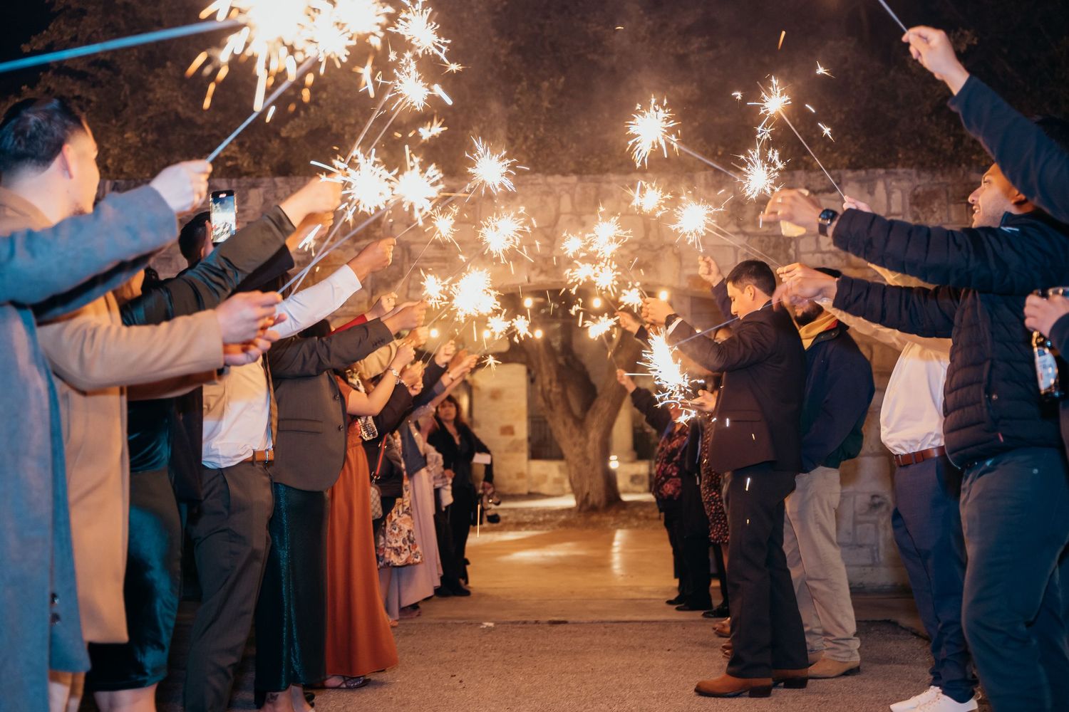 Wedding guests holding sparklers creating an illuminated tunnel for the newlyweds.