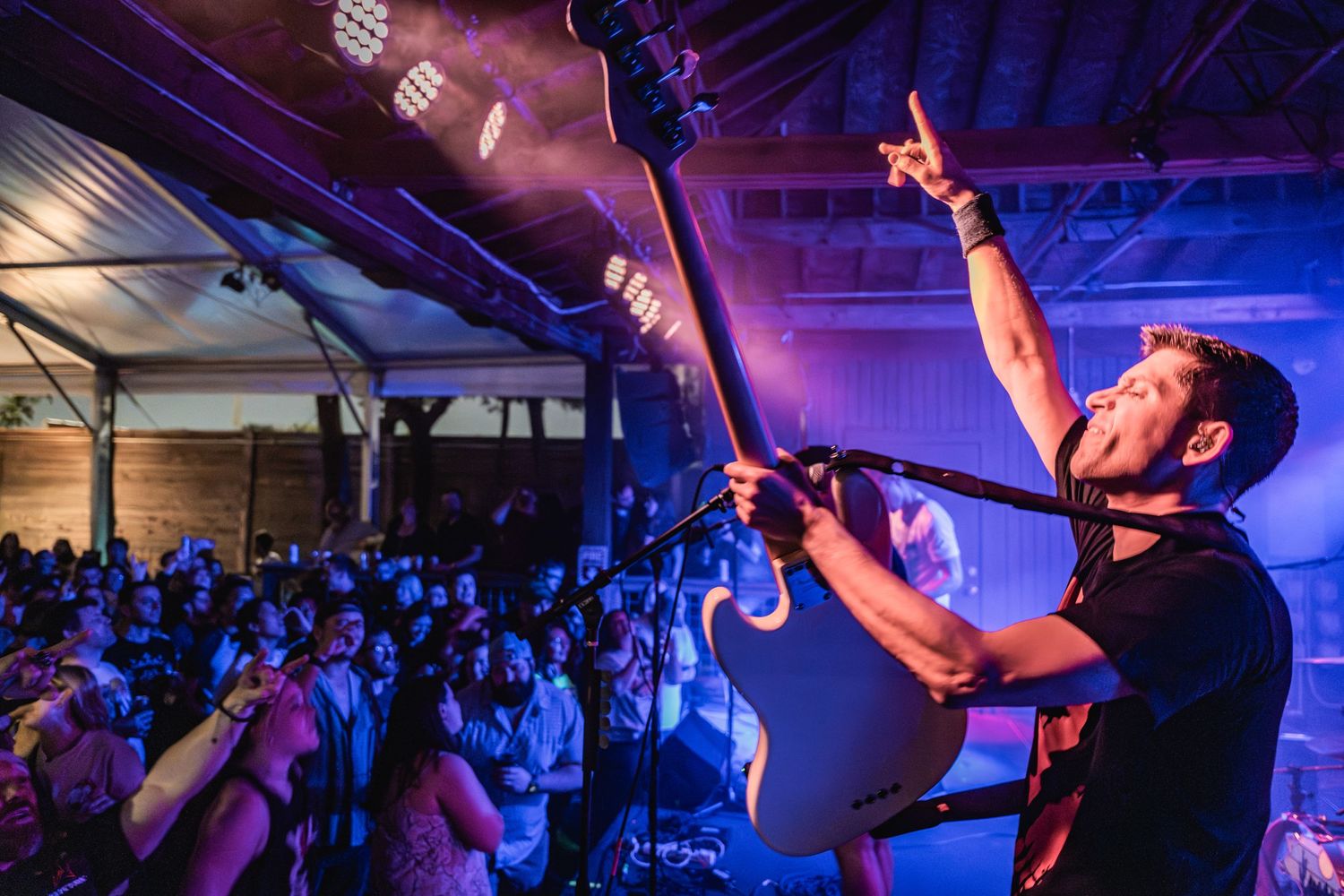 A musician performs on stage under dramatic blue lighting with a crowd visible in the background.