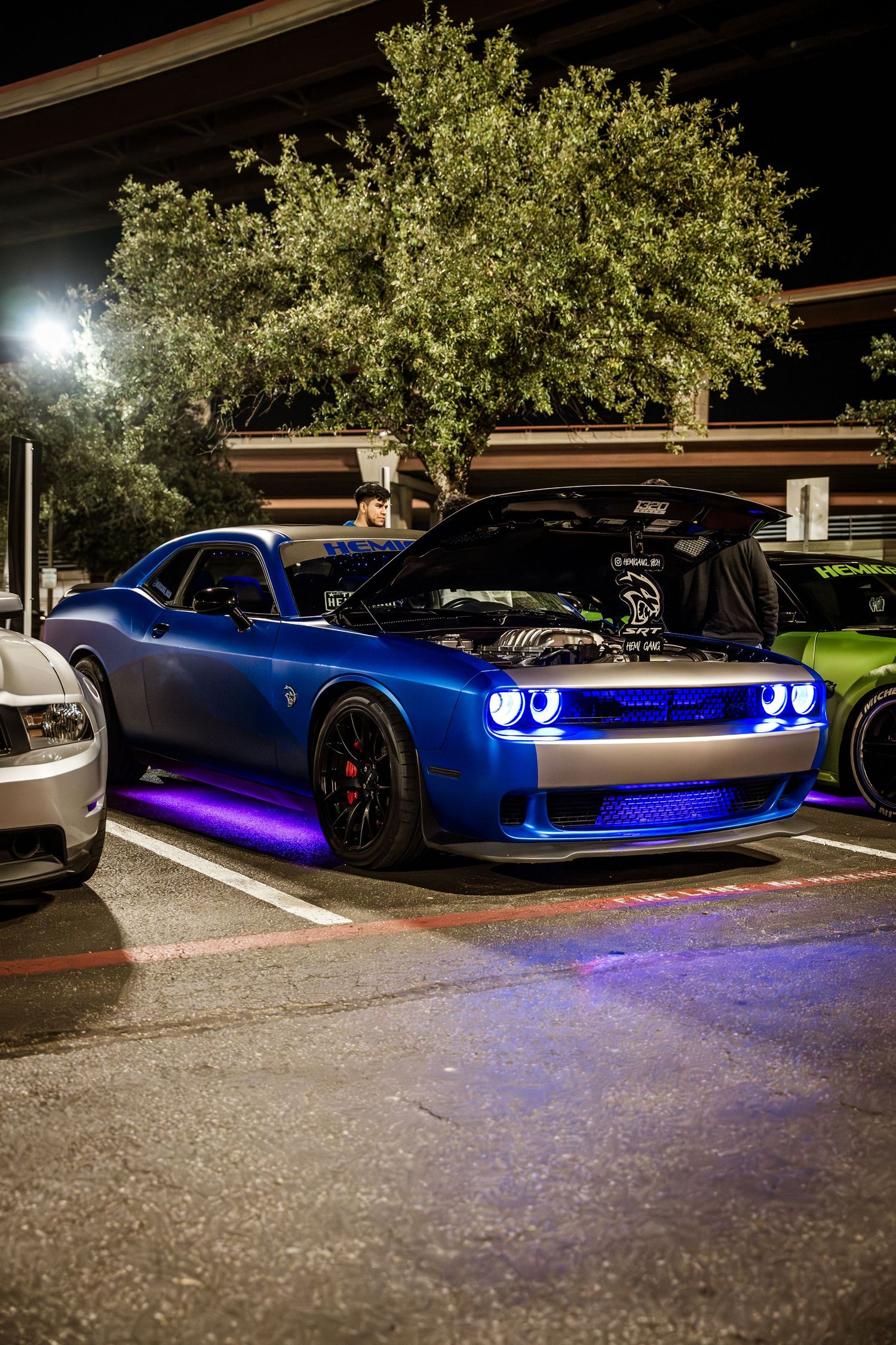 A blue Dodge Challenger with purple LED underglow lighting parked at night.