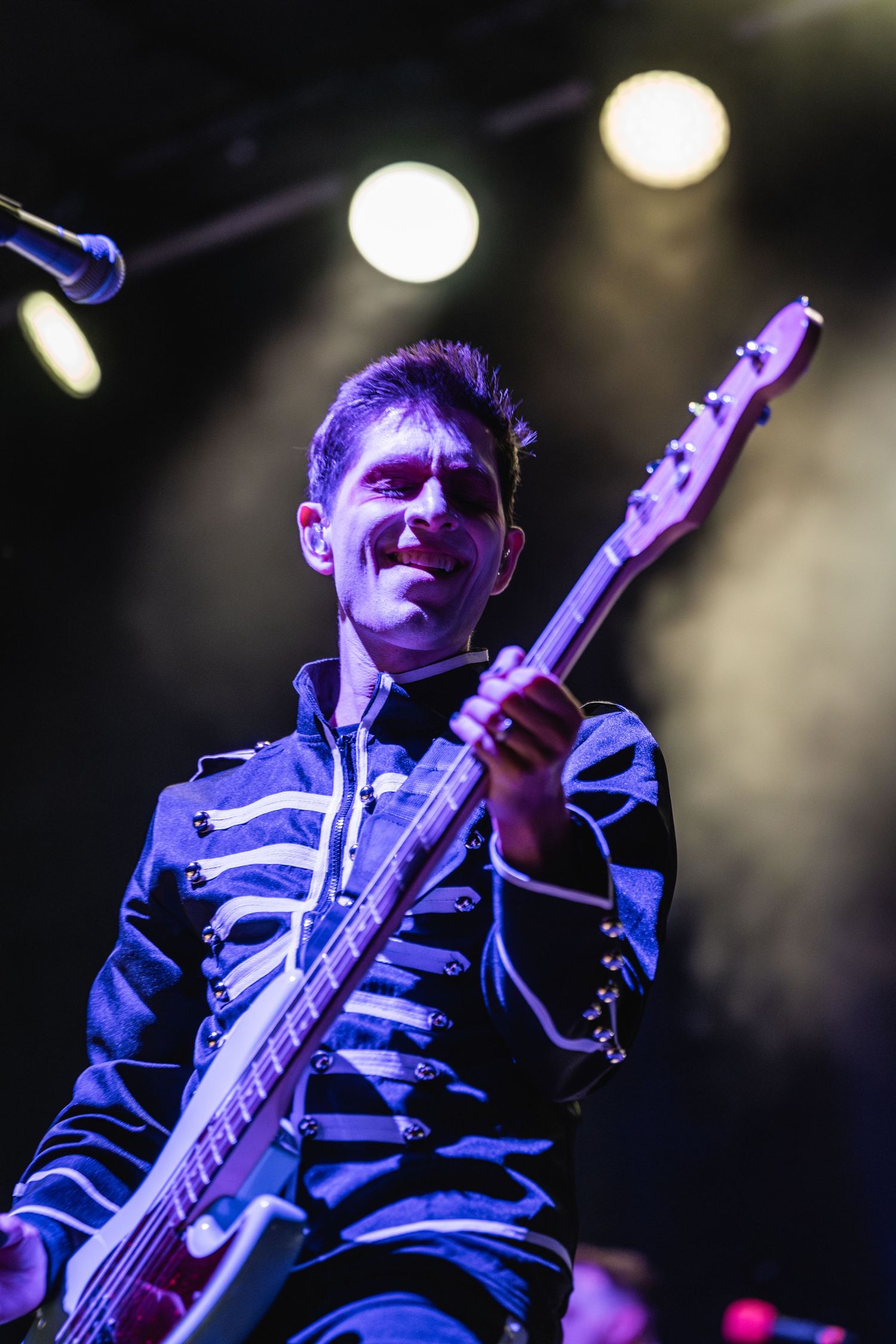Bass player in skeleton-print uniform smiling while performing under stage lights.