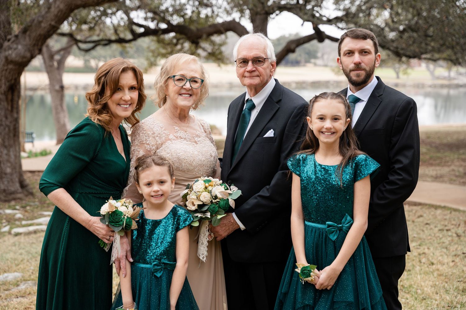 Family poses together outdoors in formal attire with matching emerald green velvet dresses and a traditional bouquet.