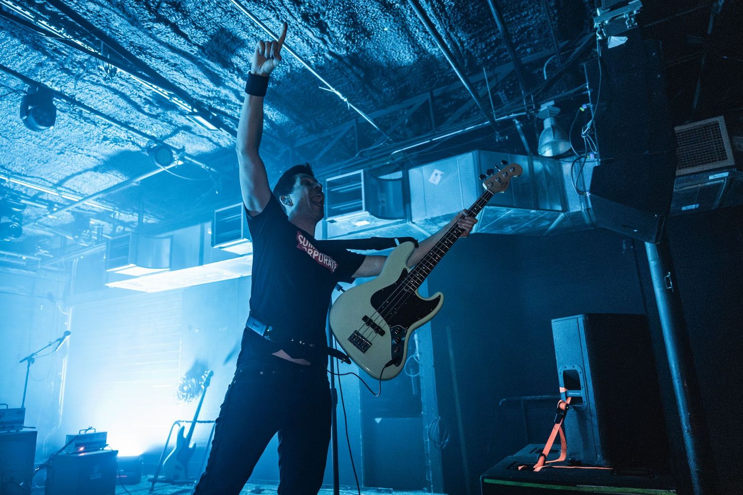 Musician performs energetically on stage with bass guitar silhouetted against bright blue concert lighting.