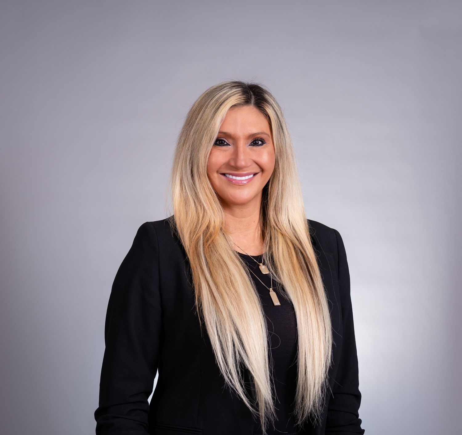 Professional headshot of a person with long blonde hair wearing a black blazer against a gray background.