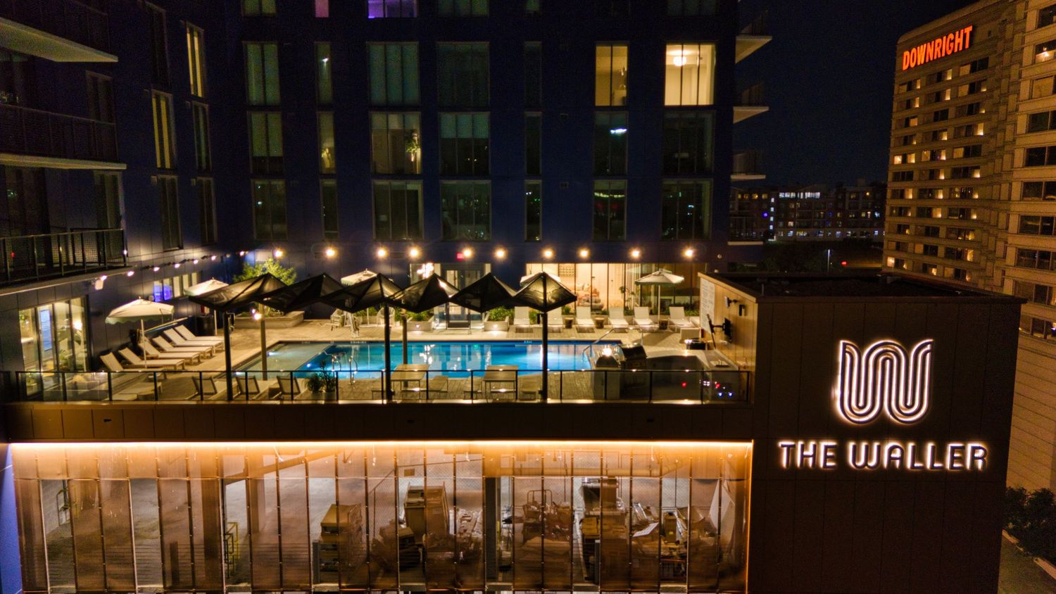 Night view of The Waller hotel's rooftop pool deck with lounge chairs and ambient lighting.