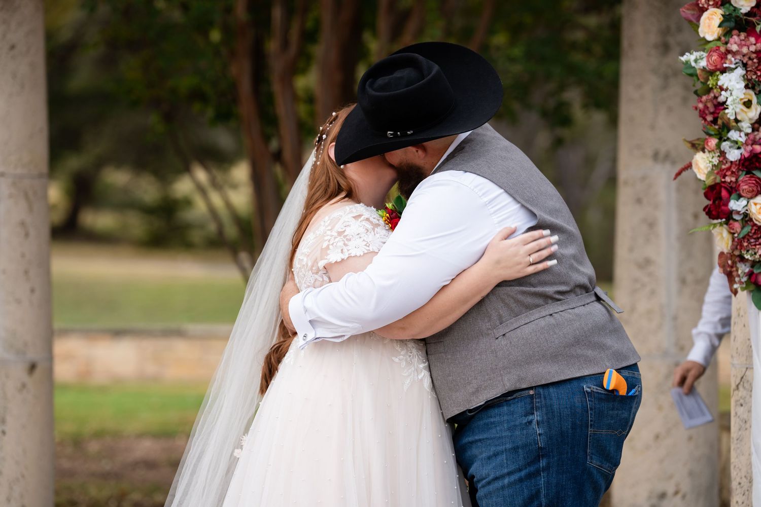 A romantic embrace during a wedding ceremony under a floral-decorated pergola.