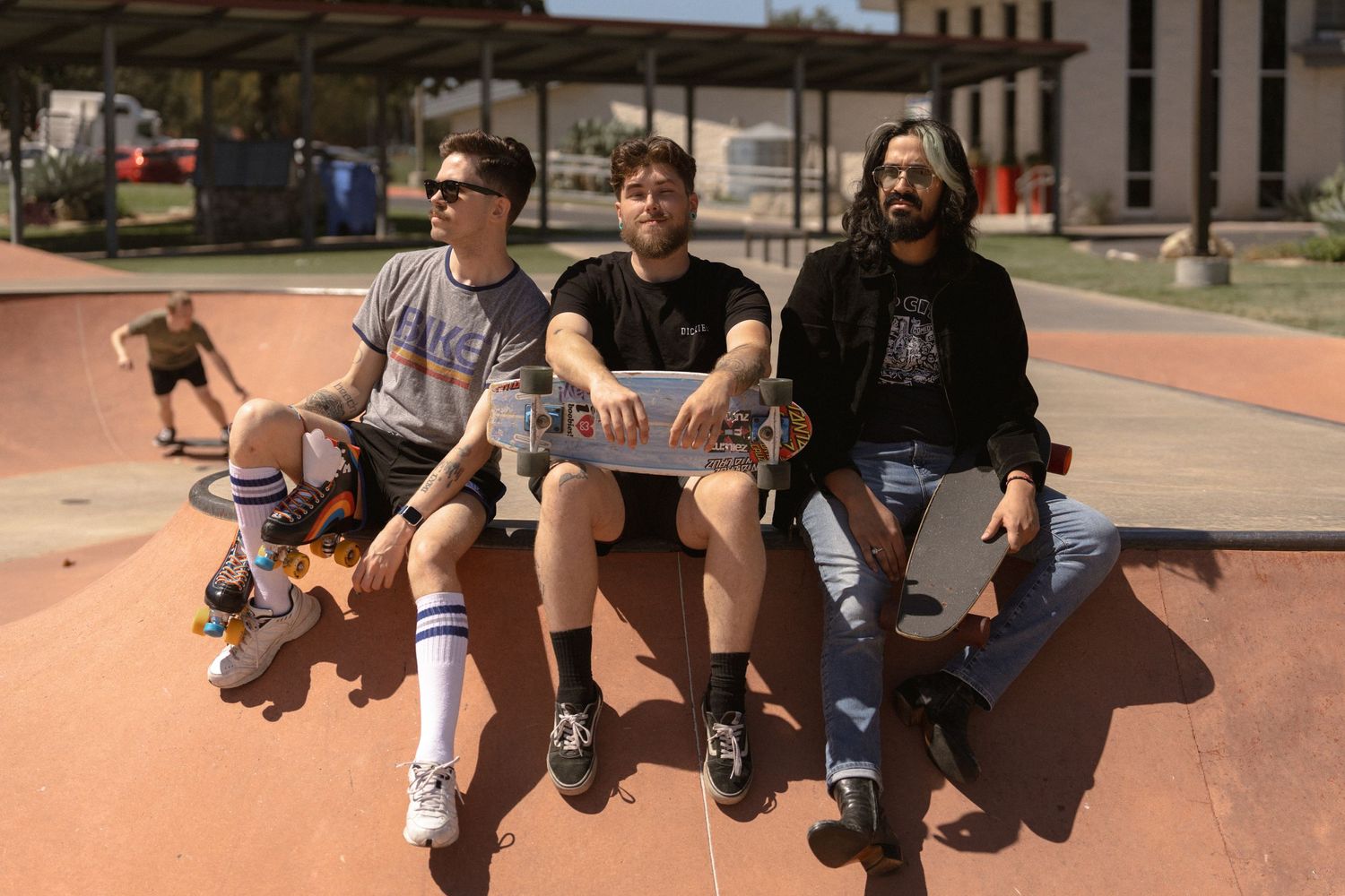 Three people sitting and chatting at outdoor skate park on sunny day.