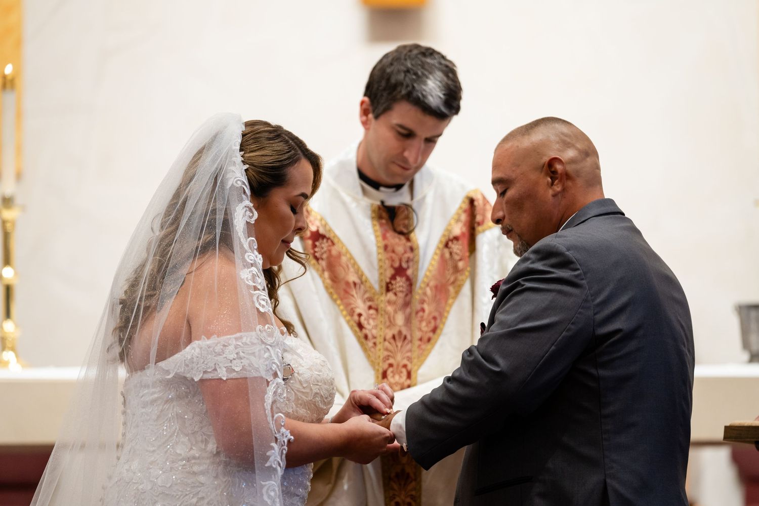 Intimate moment during wedding ceremony as couple exchanges rings at church altar.
