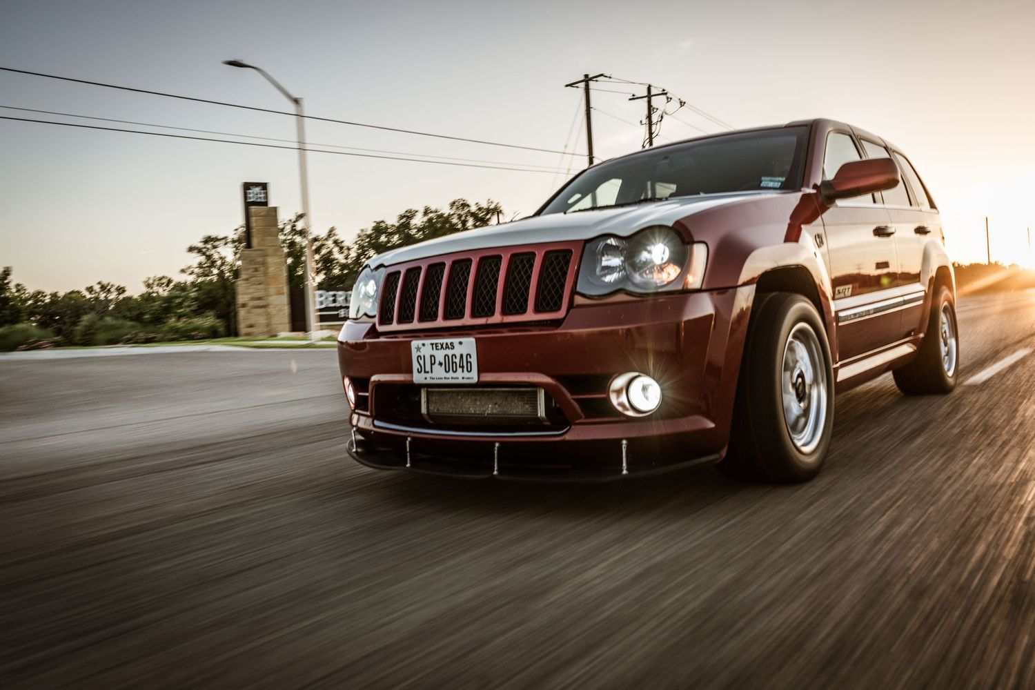 Maroon Jeep Grand Cherokee SRT8 captured in dynamic rolling shot during sunset.