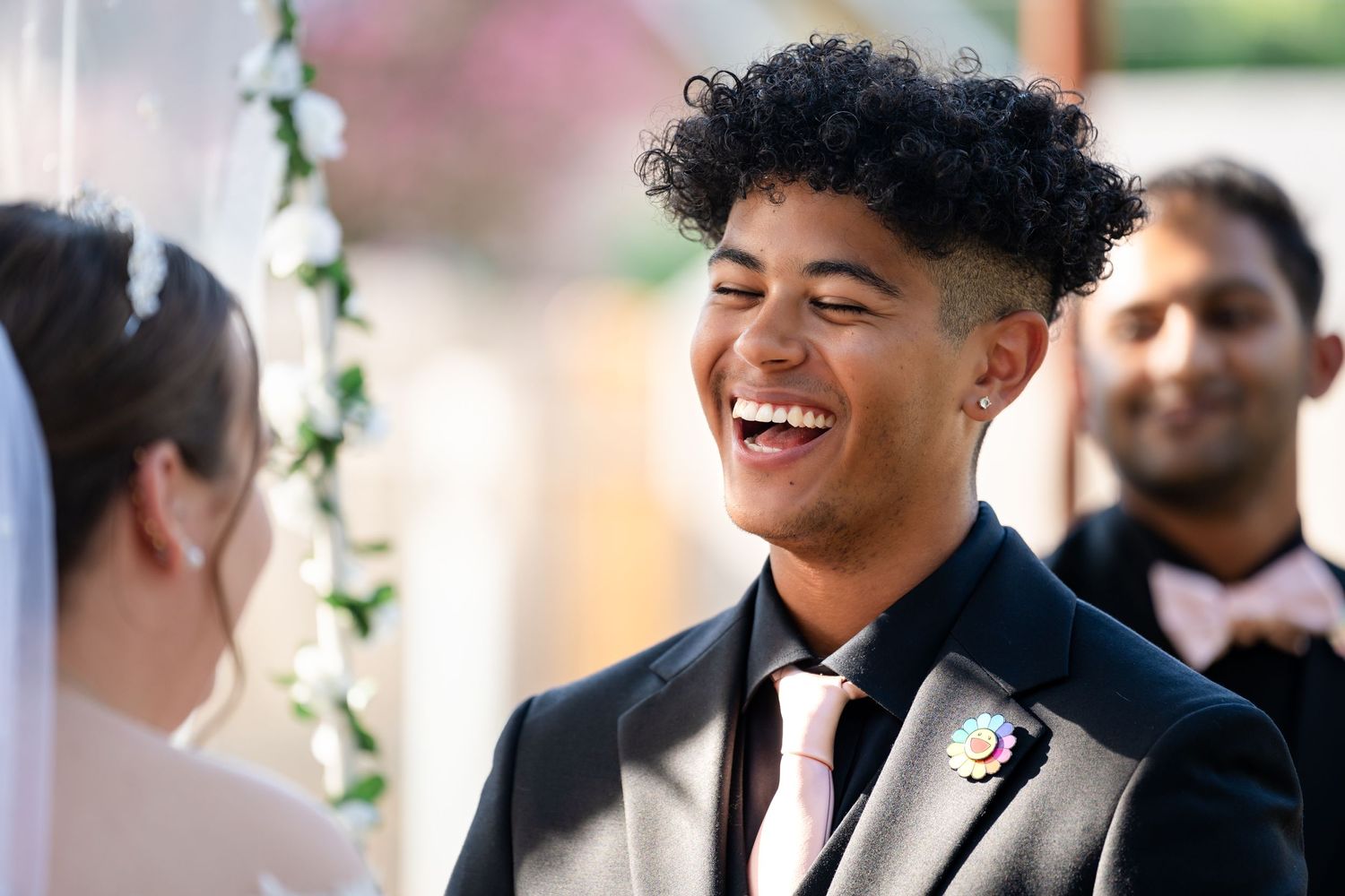 A joyous moment of laughter during an outdoor wedding ceremony under a floral arch.