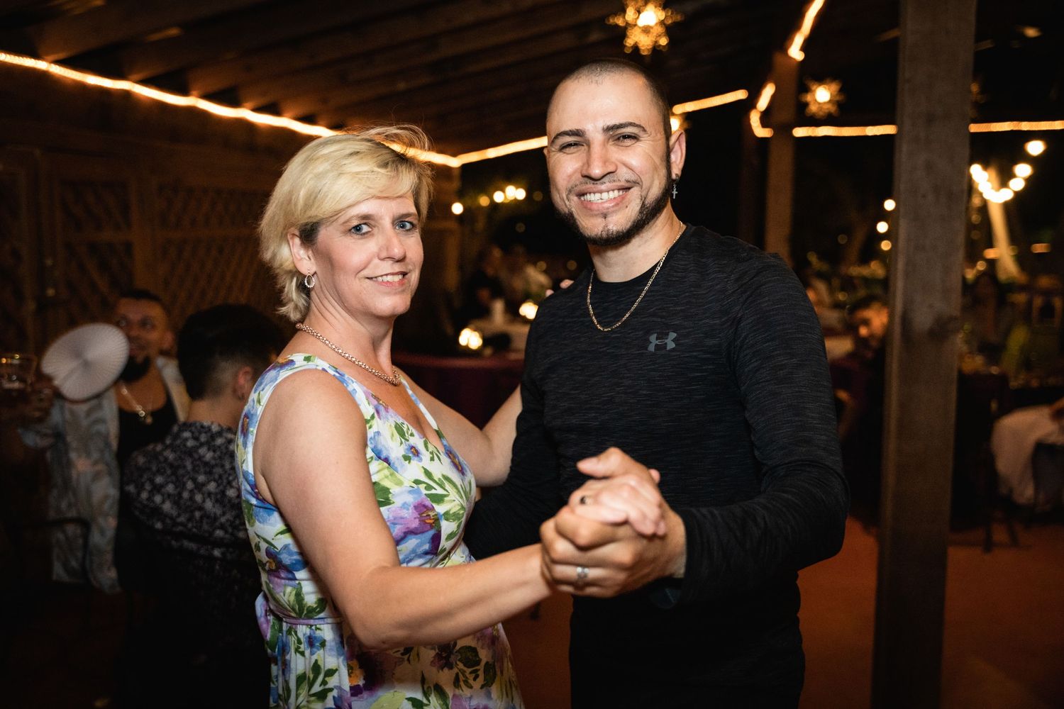 Two people dance together at an evening reception under string lights.