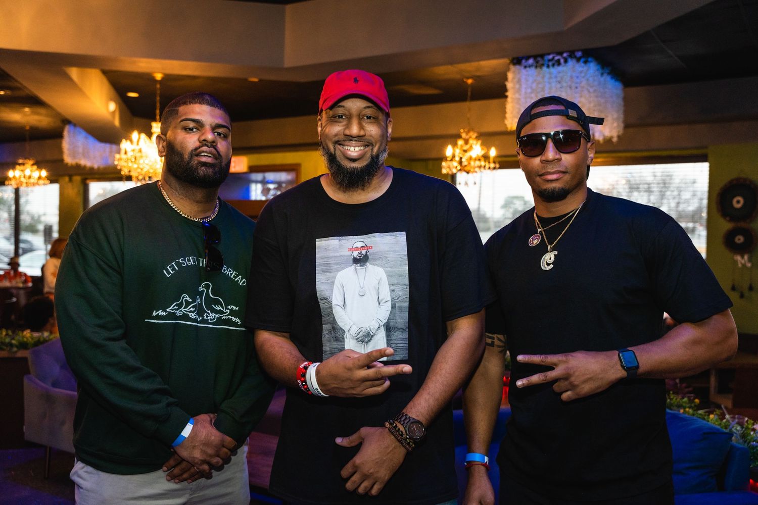 Three friends pose together at a dimly lit venue with warm lighting and bar decor.