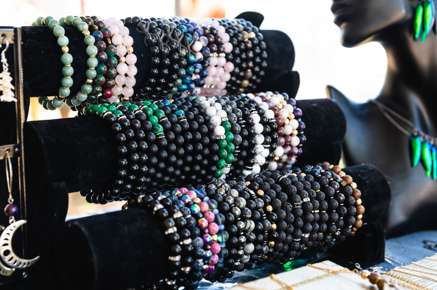 Beaded bracelets and jewelry displayed on black velvet stands at market stall.