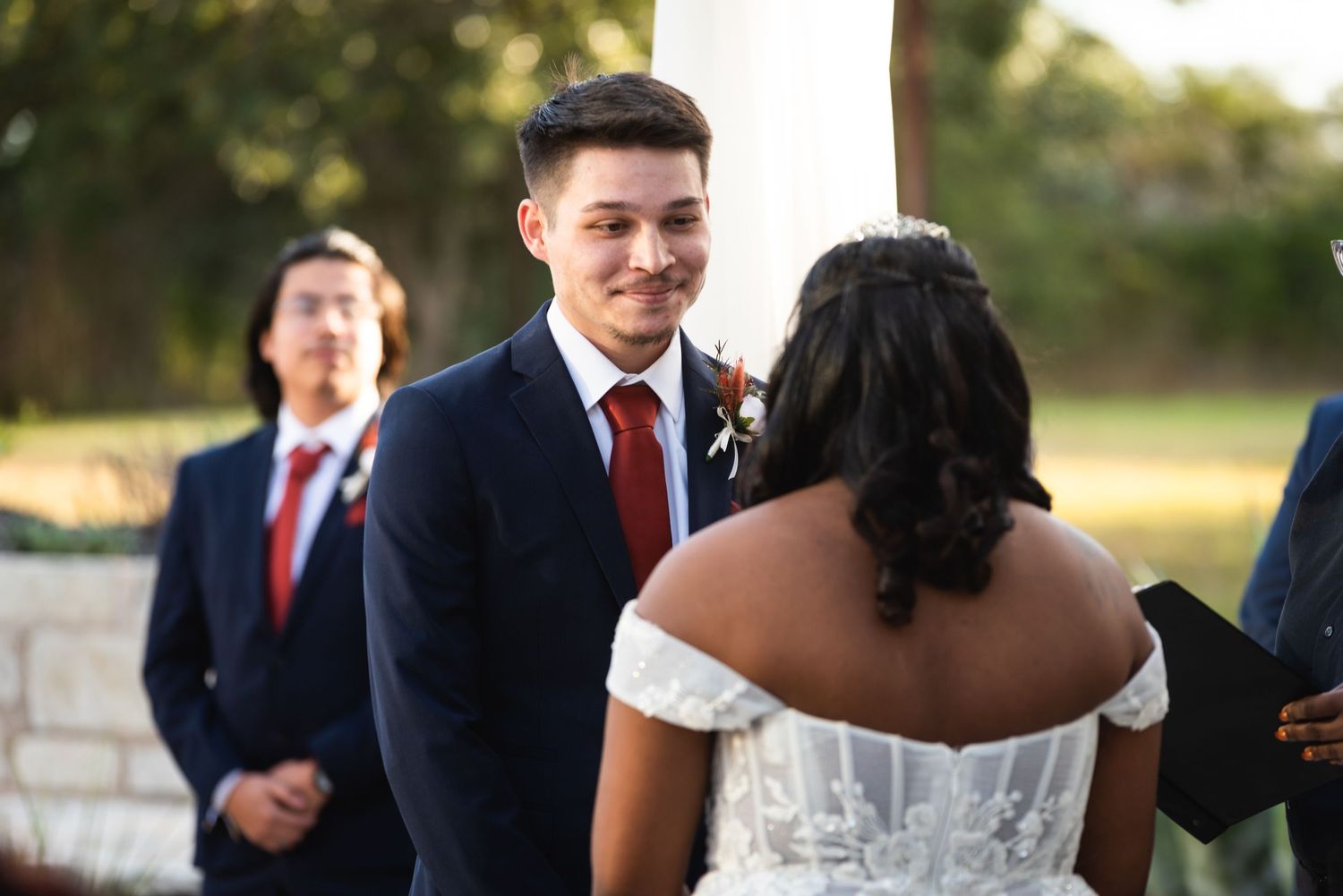 A wedding ceremony takes place outdoors with the groom and bride in formal attire at the altar.