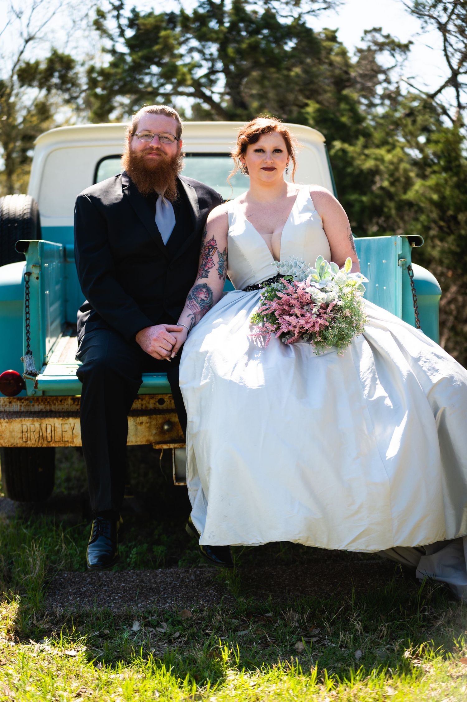 A couple sits together on a vintage turquoise pickup truck on their wedding day.