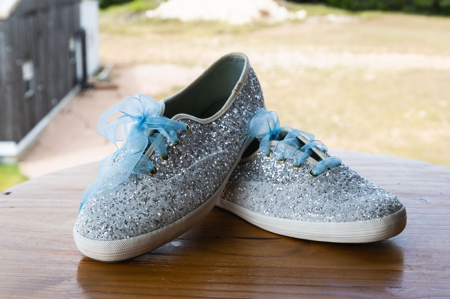 Sparkly silver sneakers with light blue laces sit on a wooden surface.