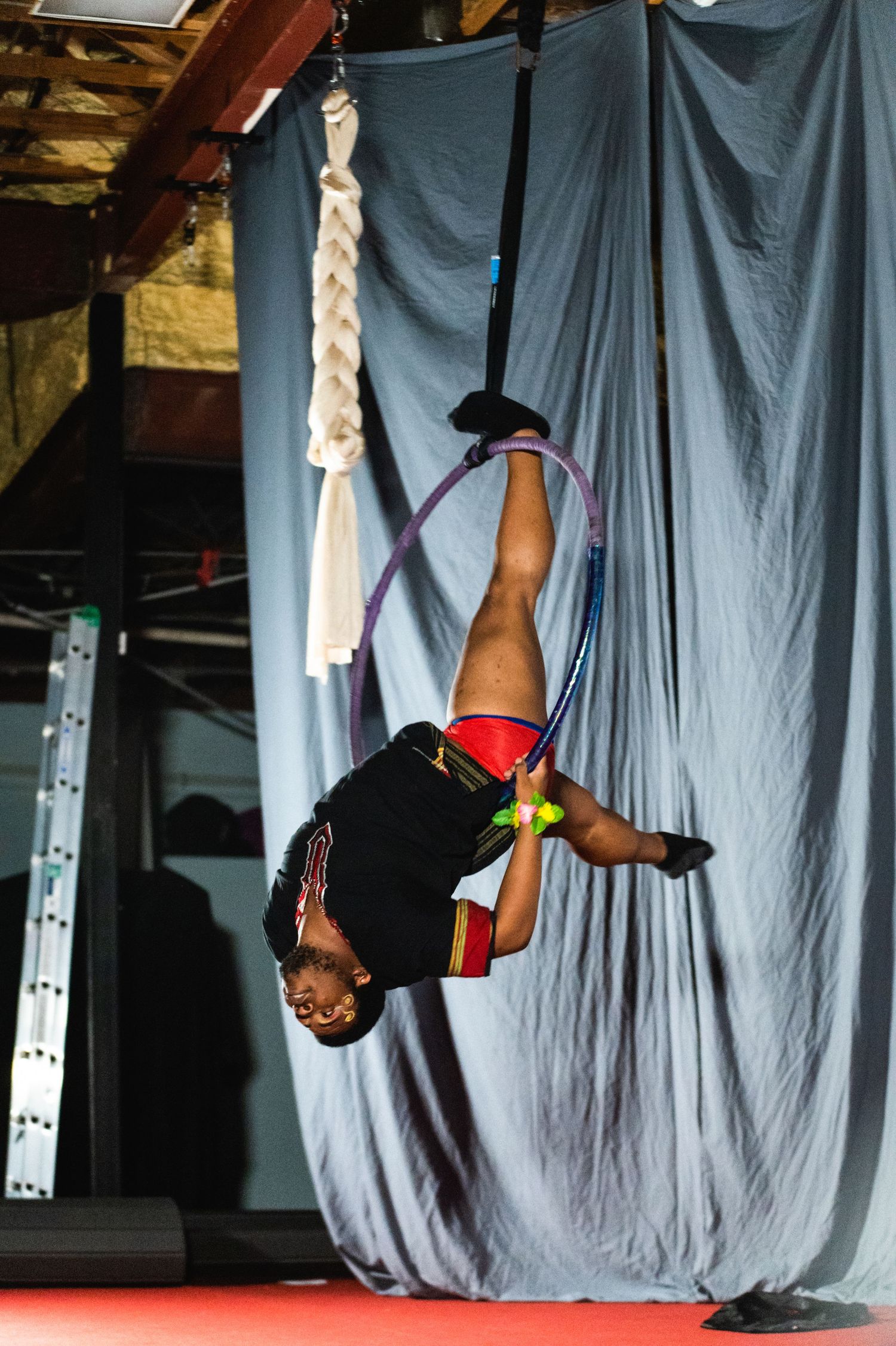 A performer hangs upside down on aerial silks against a grey backdrop during an acrobatic routine.