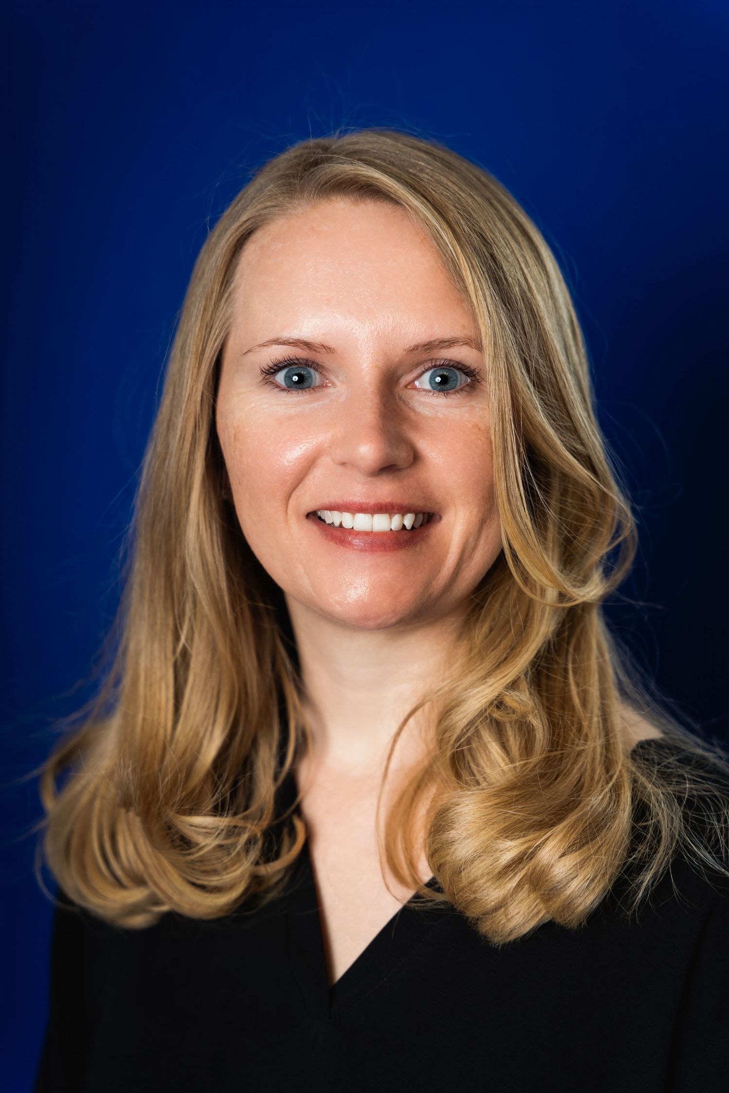 Professional headshot of a person in a black top against a deep blue background.