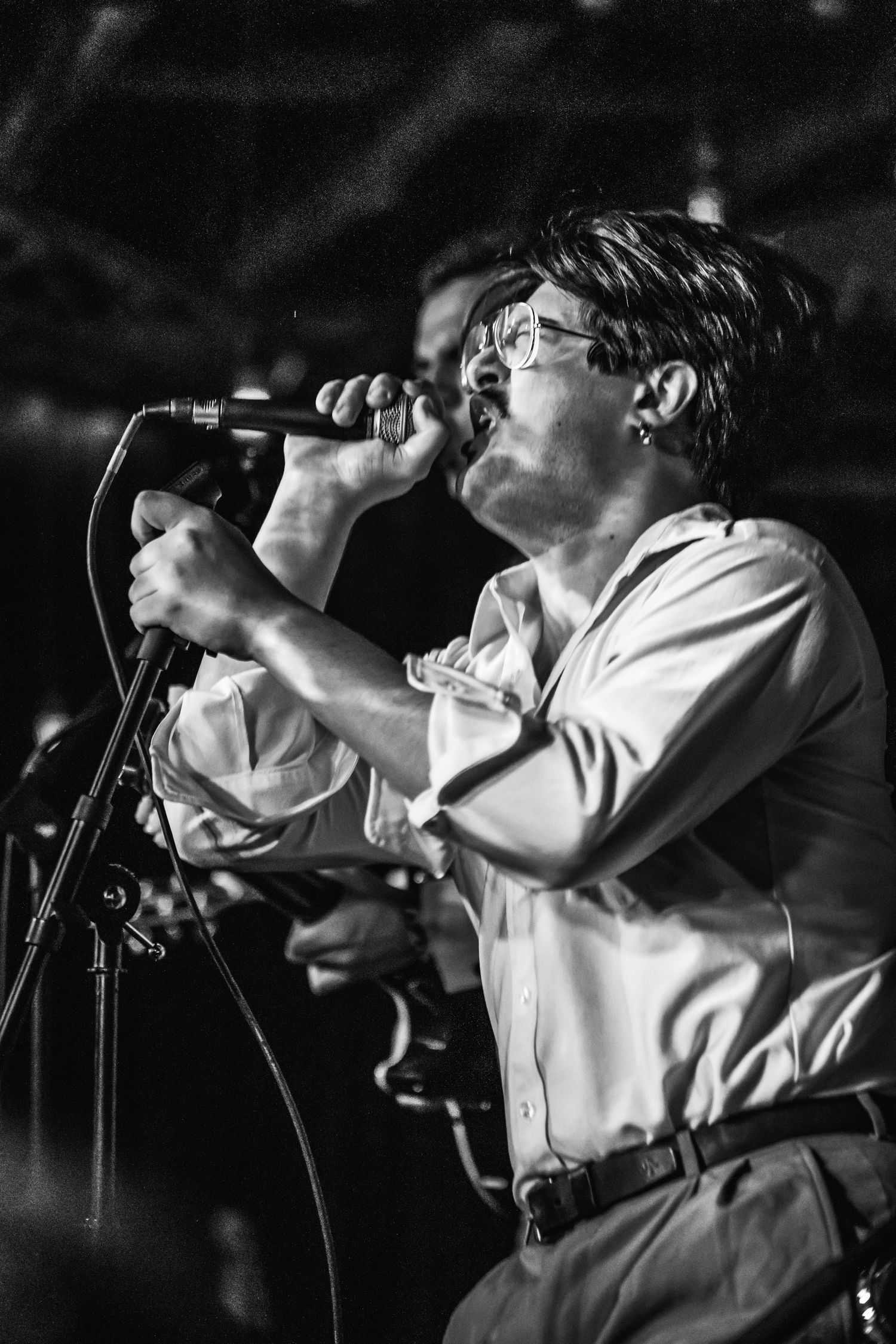 A performer passionately singing into a microphone during a dramatic black and white stage performance.