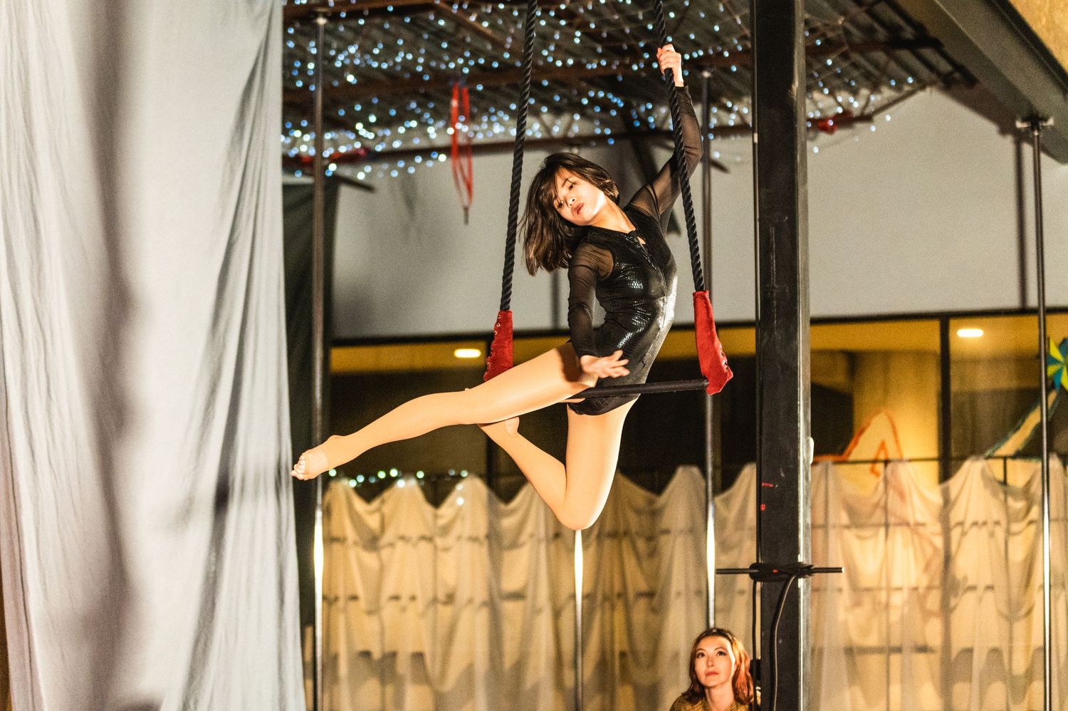 Performer executing a split pose while suspended from aerial equipment.
