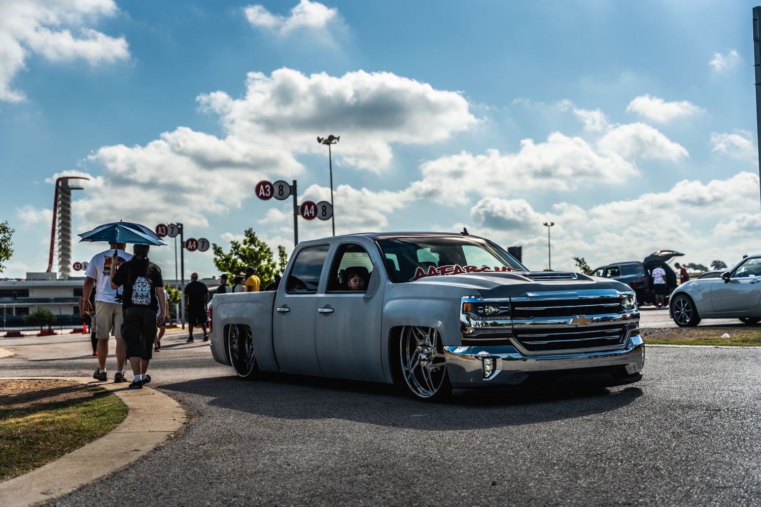Lowered grey Chevrolet Silverado pickup truck at a car meet under cloudy skies.