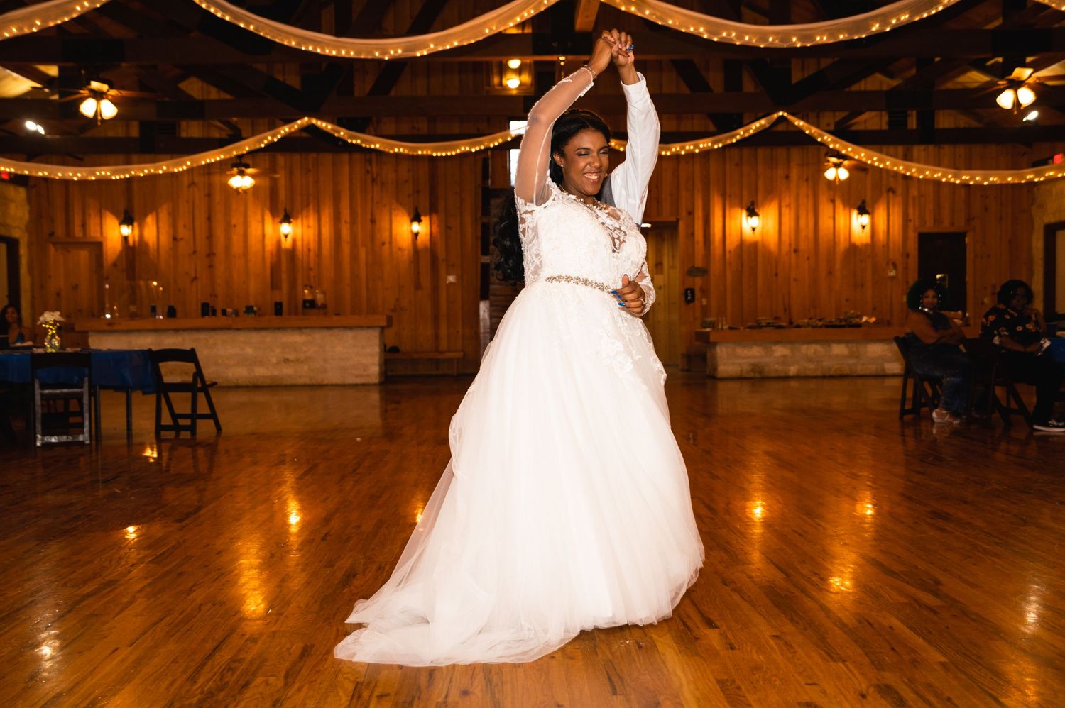 A bride in a flowing white gown dances solo under elegant draping and warm lighting at a reception venue.