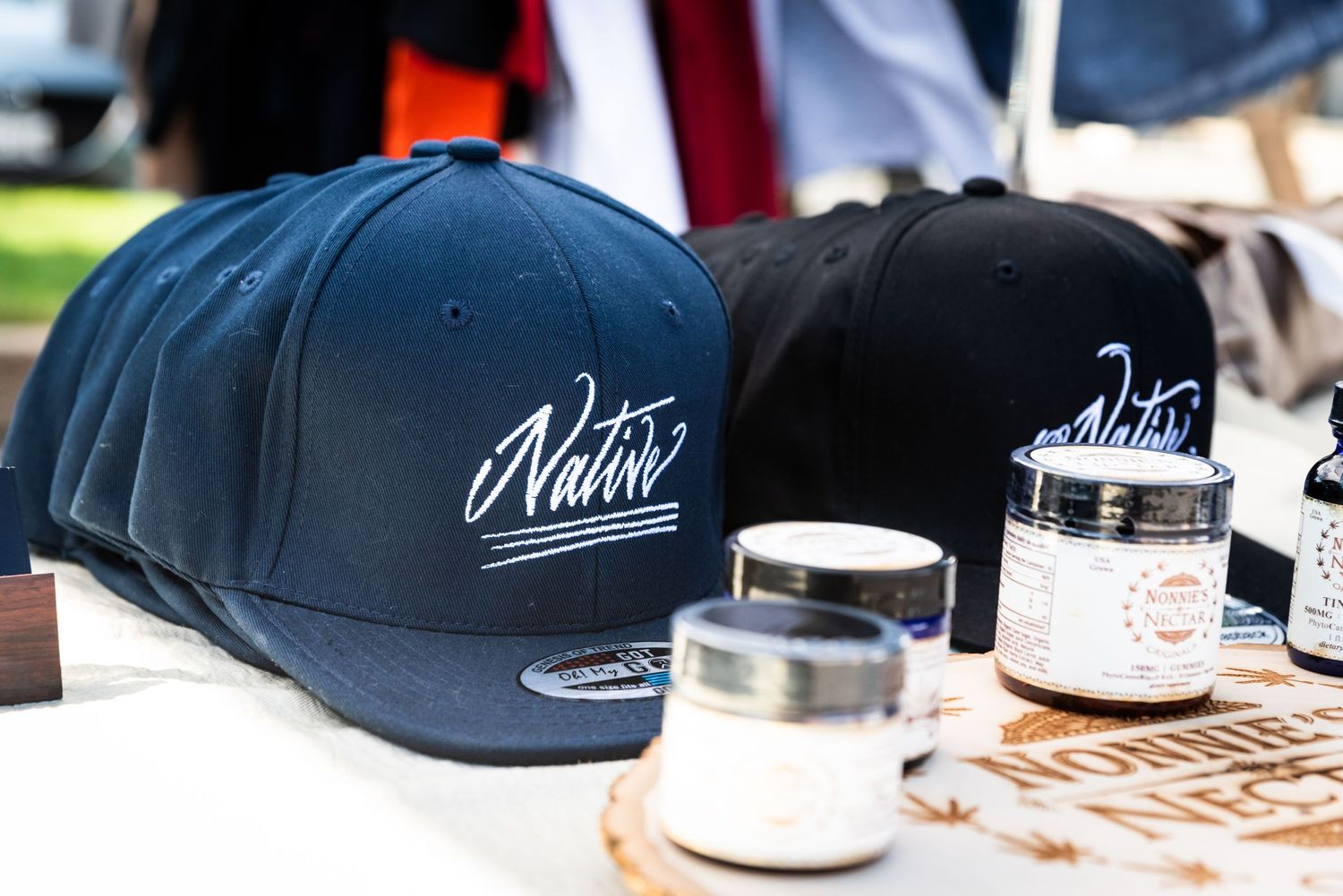 Black snapback hats with white Native logo displayed with product jars at market stand.