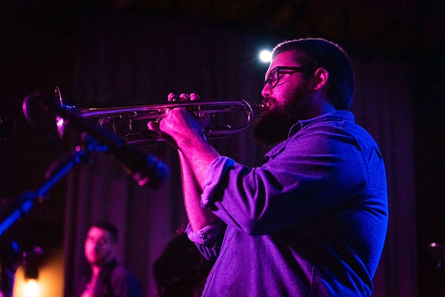 Trumpet player performs under blue stage lighting during a live jazz performance.
