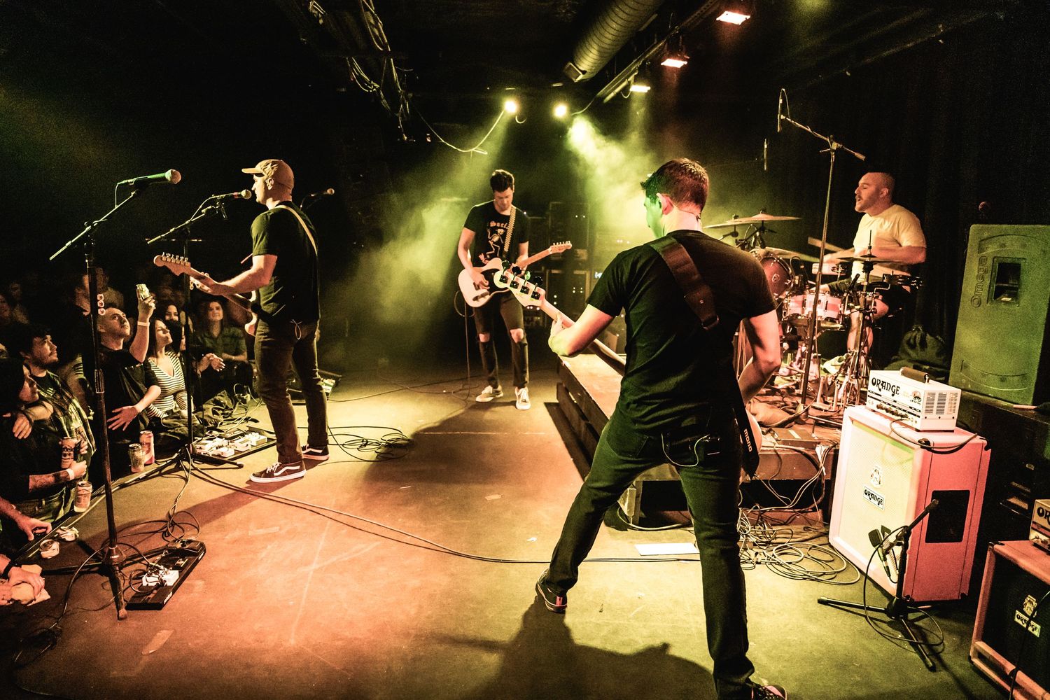 Band members perform energetically on stage with yellow lighting and fog effects.