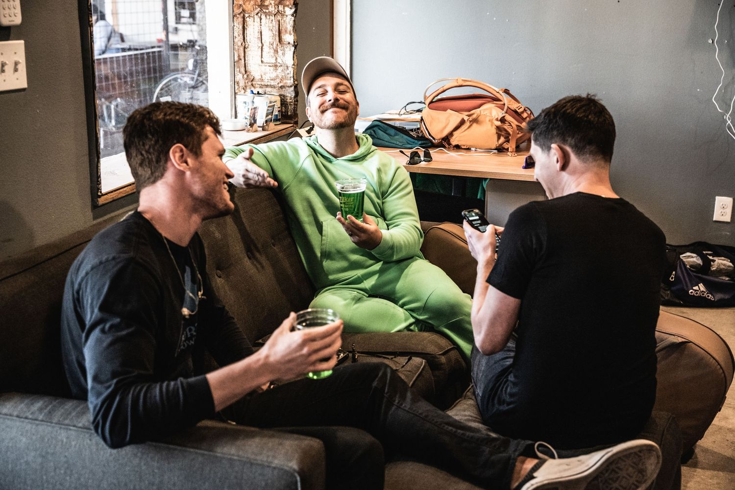 Three friends enjoying conversation and laughter while relaxing on a grey couch indoors.